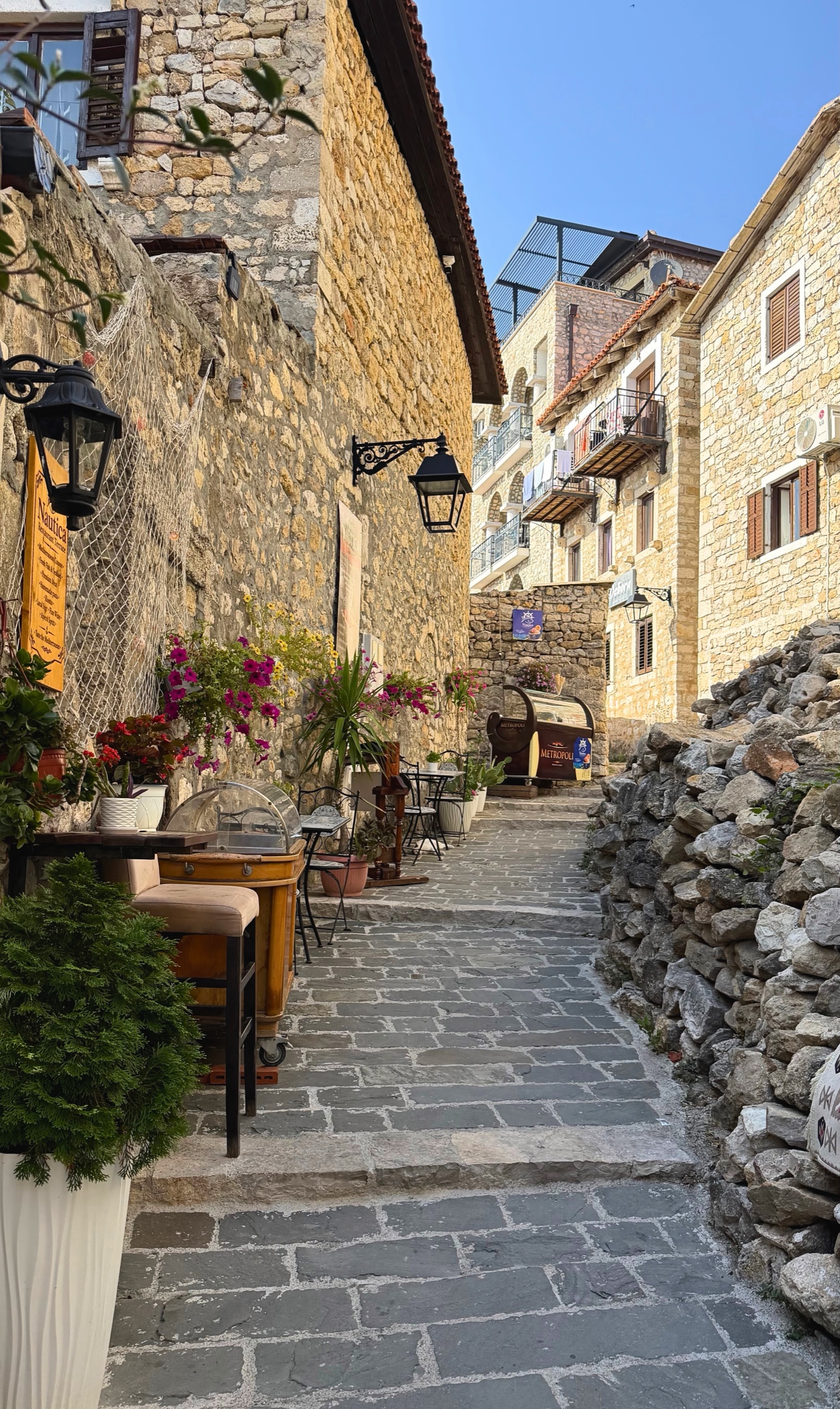 A stone lane inside Ulcinj Old Town with cafés, balconies, and flowering vines.