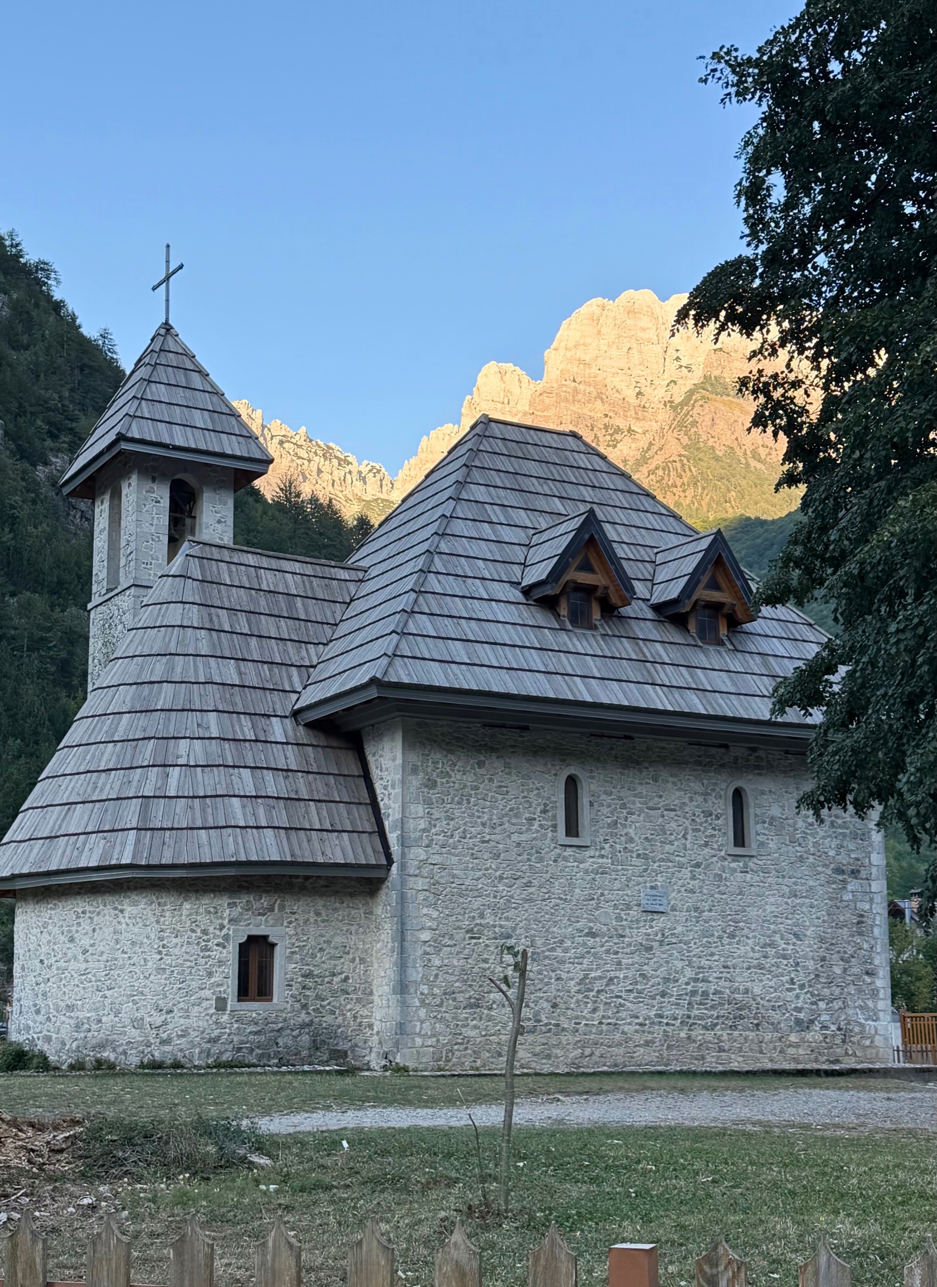 The stone Church of Theth with sunlit mountain peaks rising behind it.