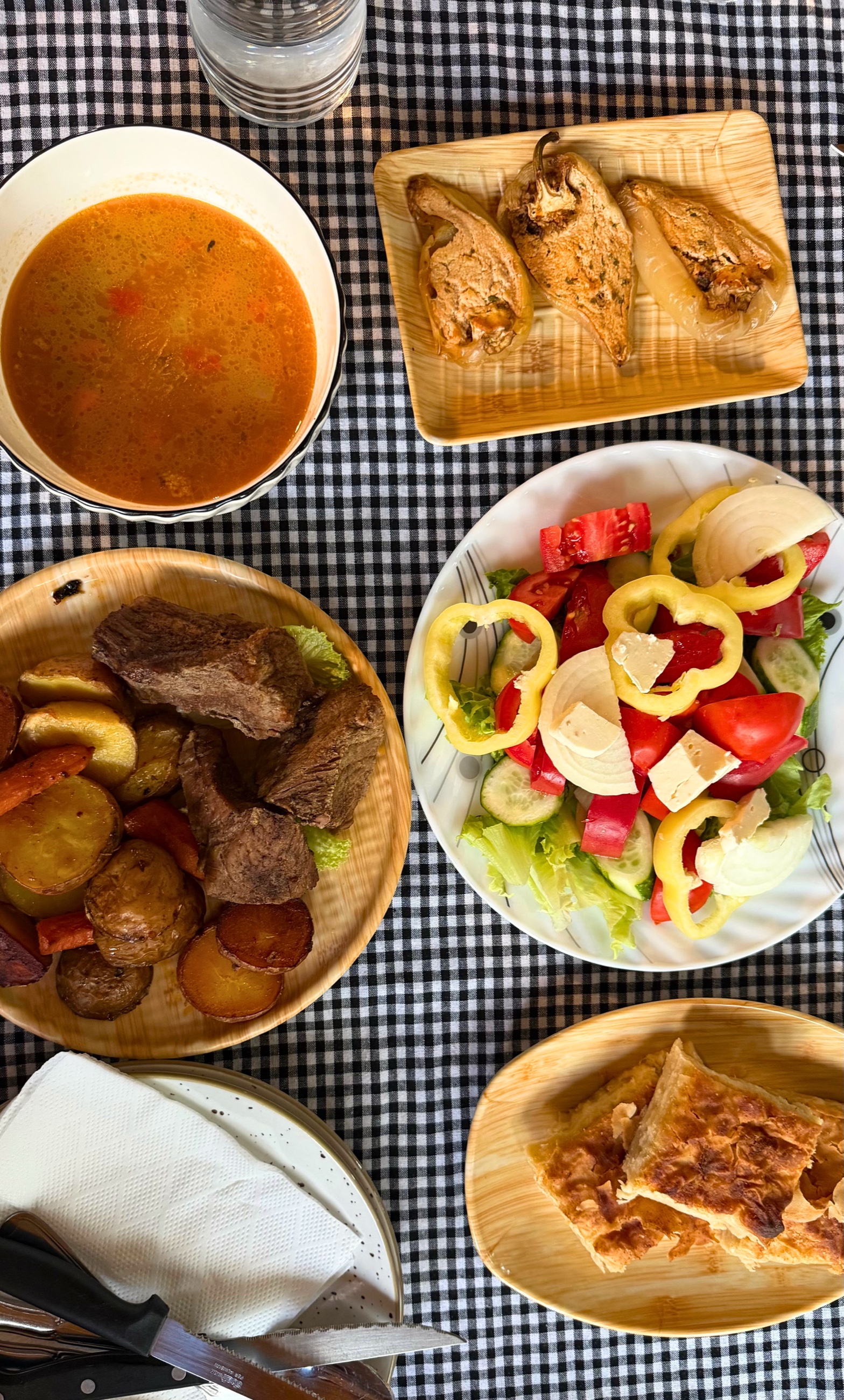 A communal mountain meal with roasted meat, potatoes, soup, stuffed peppers, salad, and cheese burek.