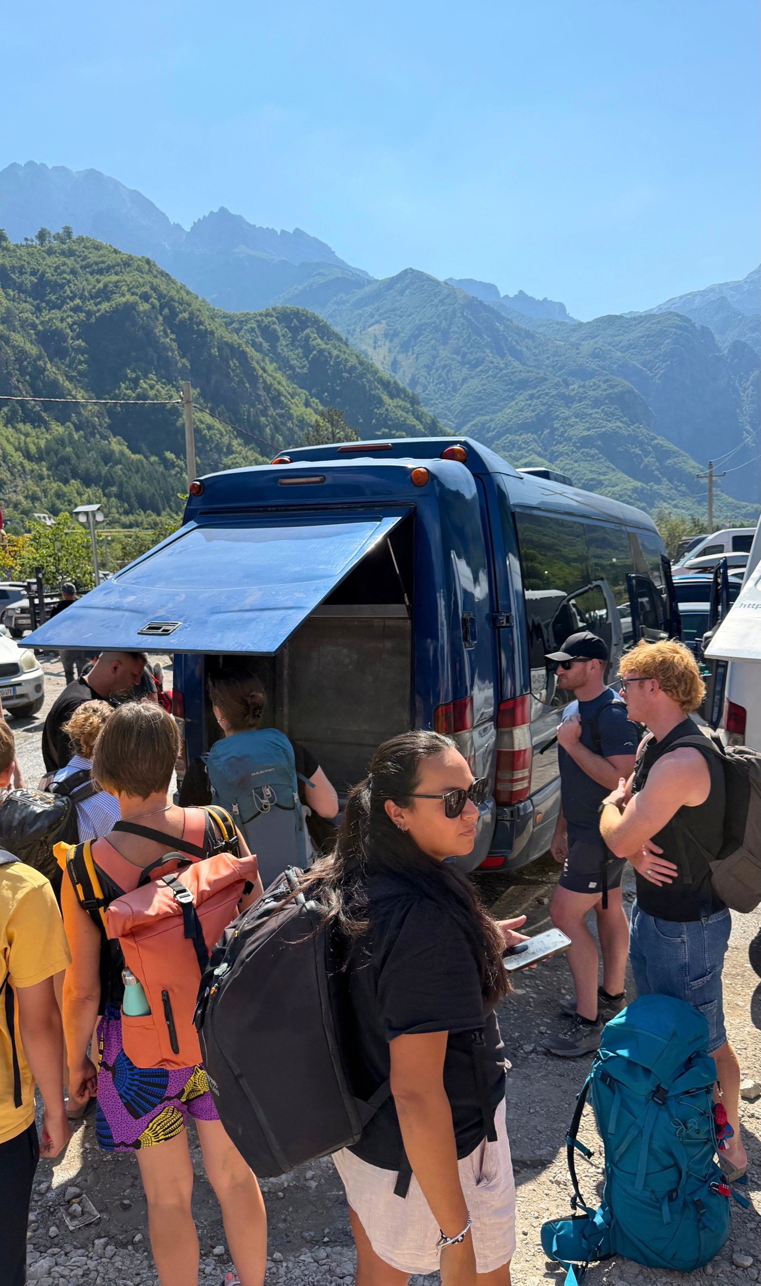 Hikers and luggage gathering around a blue van for the return trip from Theth to Tirana.