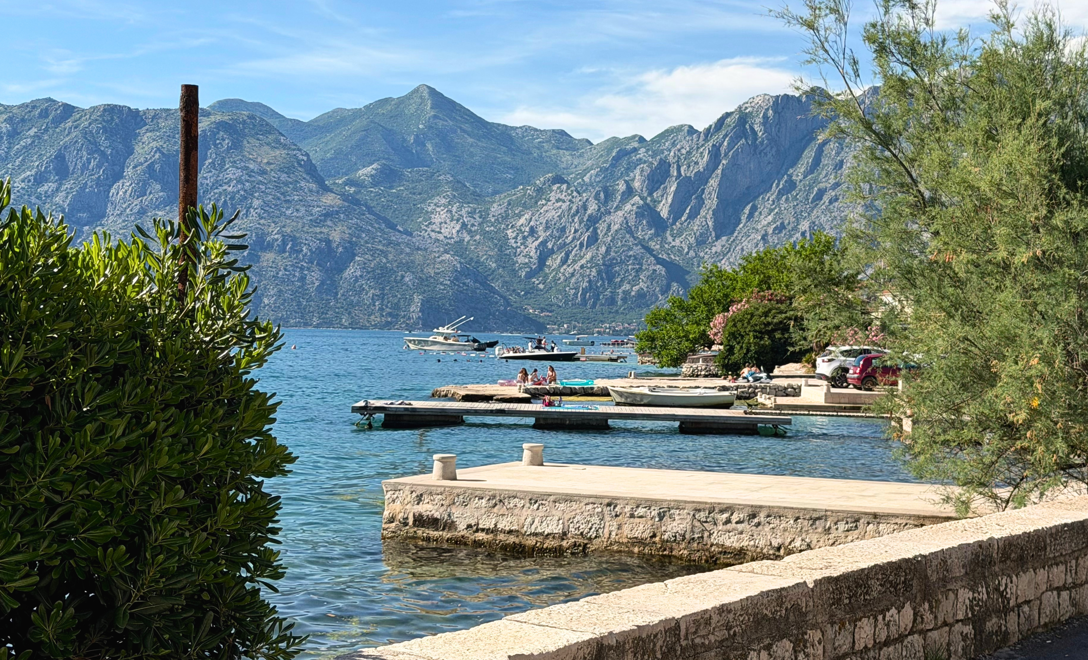 A quiet stretch of the Dobrota shoreline along the Bay of Kotor, calm water beside the promenade.