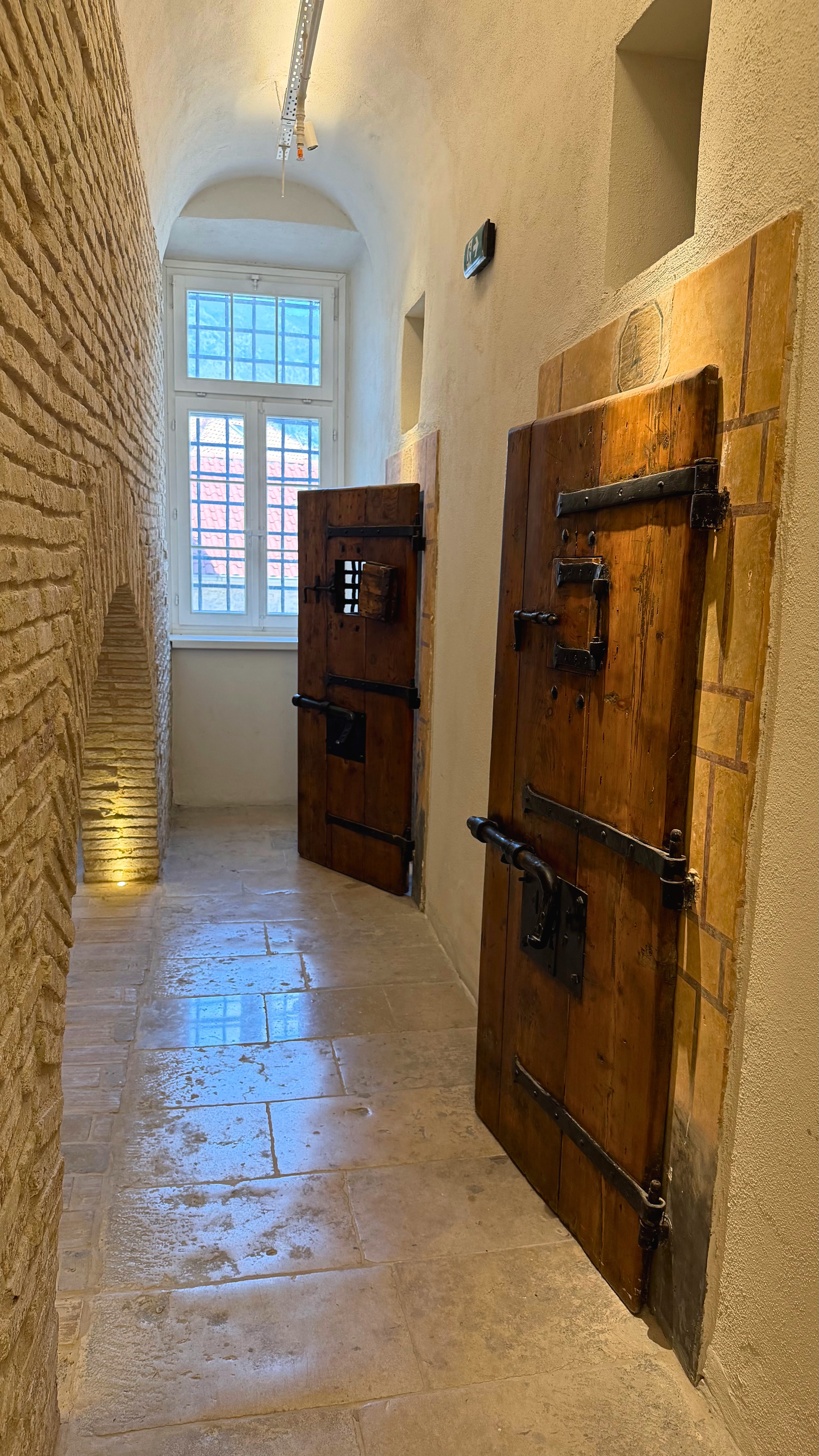 A stone corridor inside the Old Kotor Prison, heavy wooden doors leading toward artisan workshops.