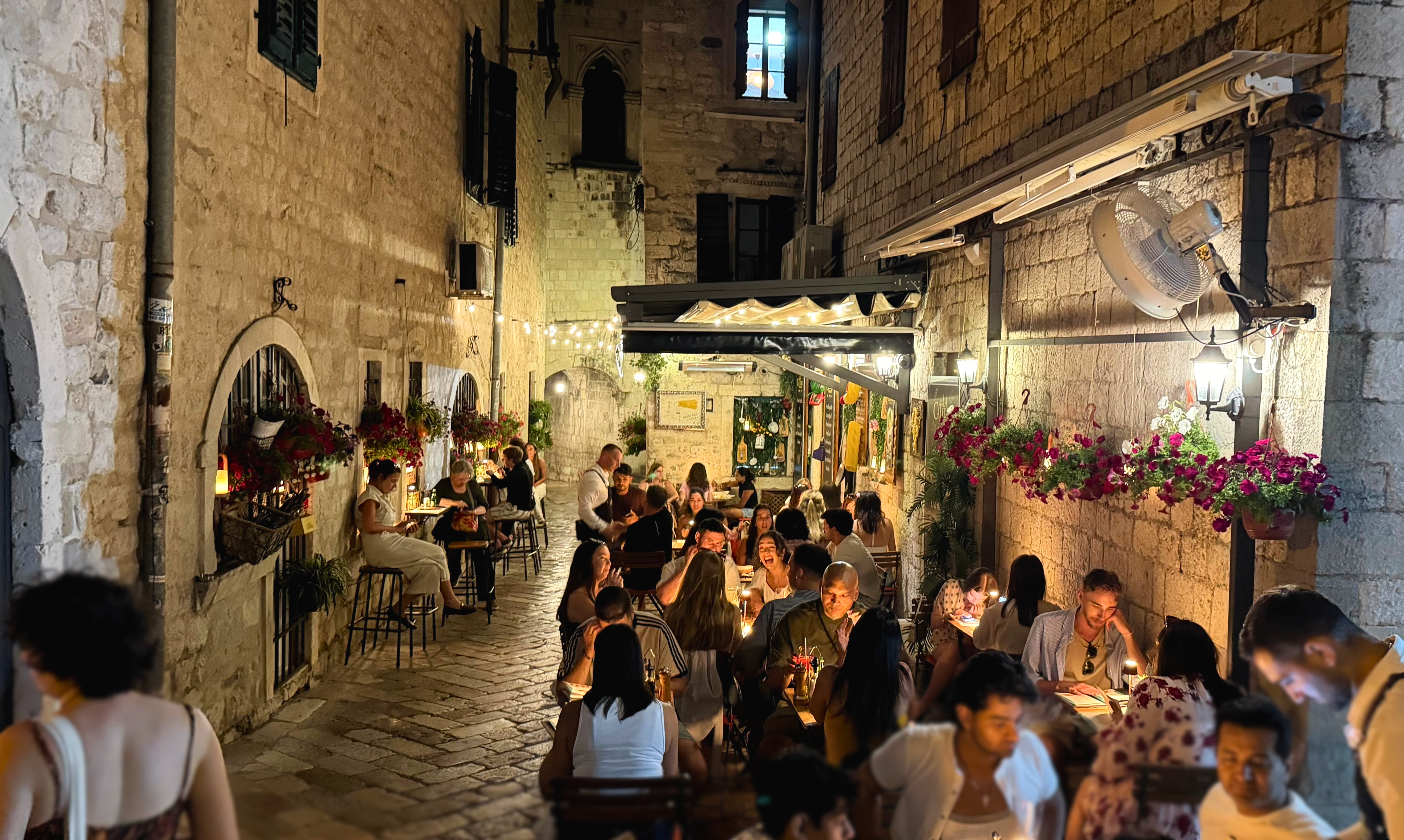 Dinner tables in a narrow stone alley behind the cathedral in Kotor Old Town after dark.