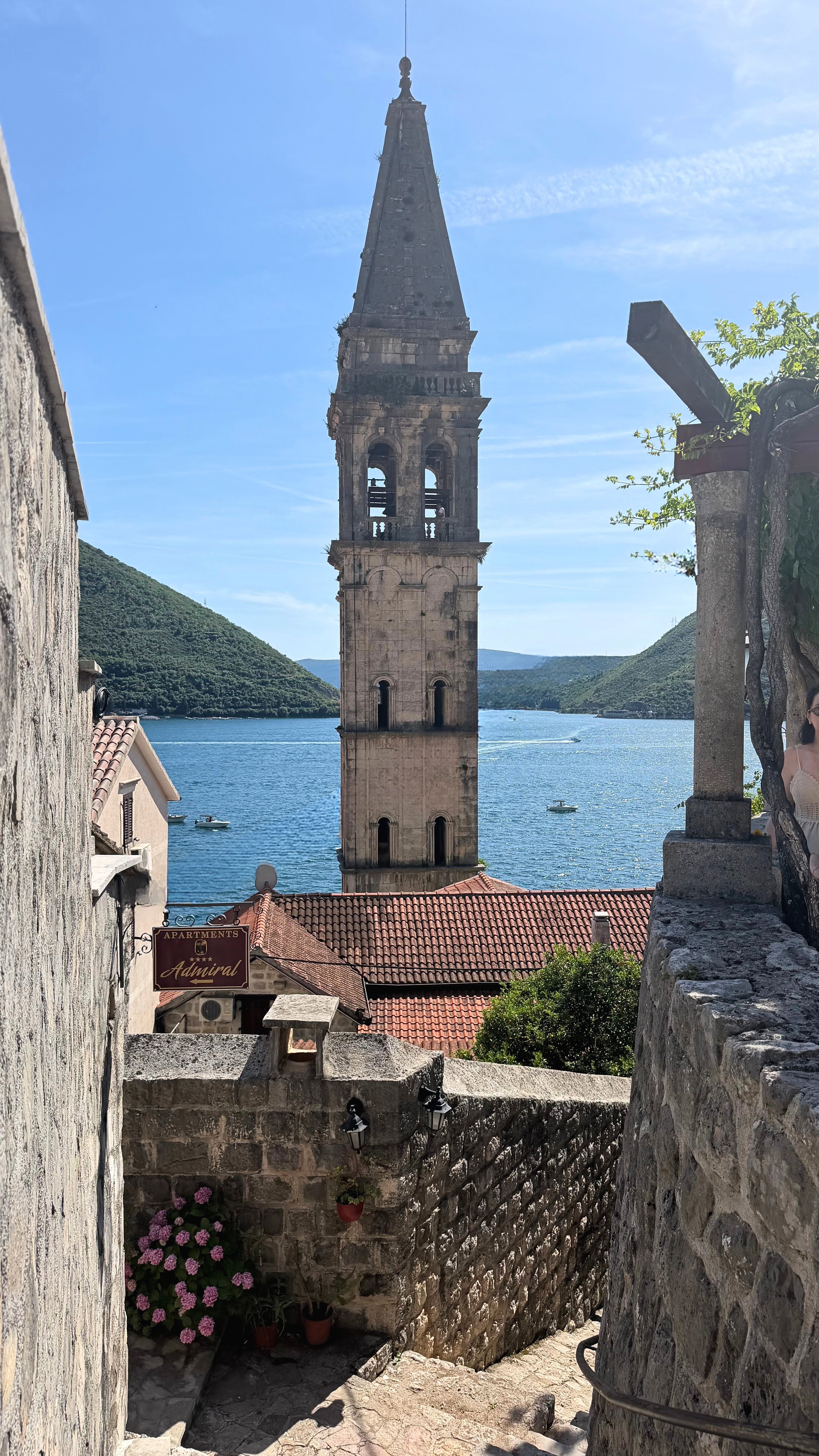 A stone stairway in Perast, with the 17th-century bell tower above the roofs and the bay beyond.