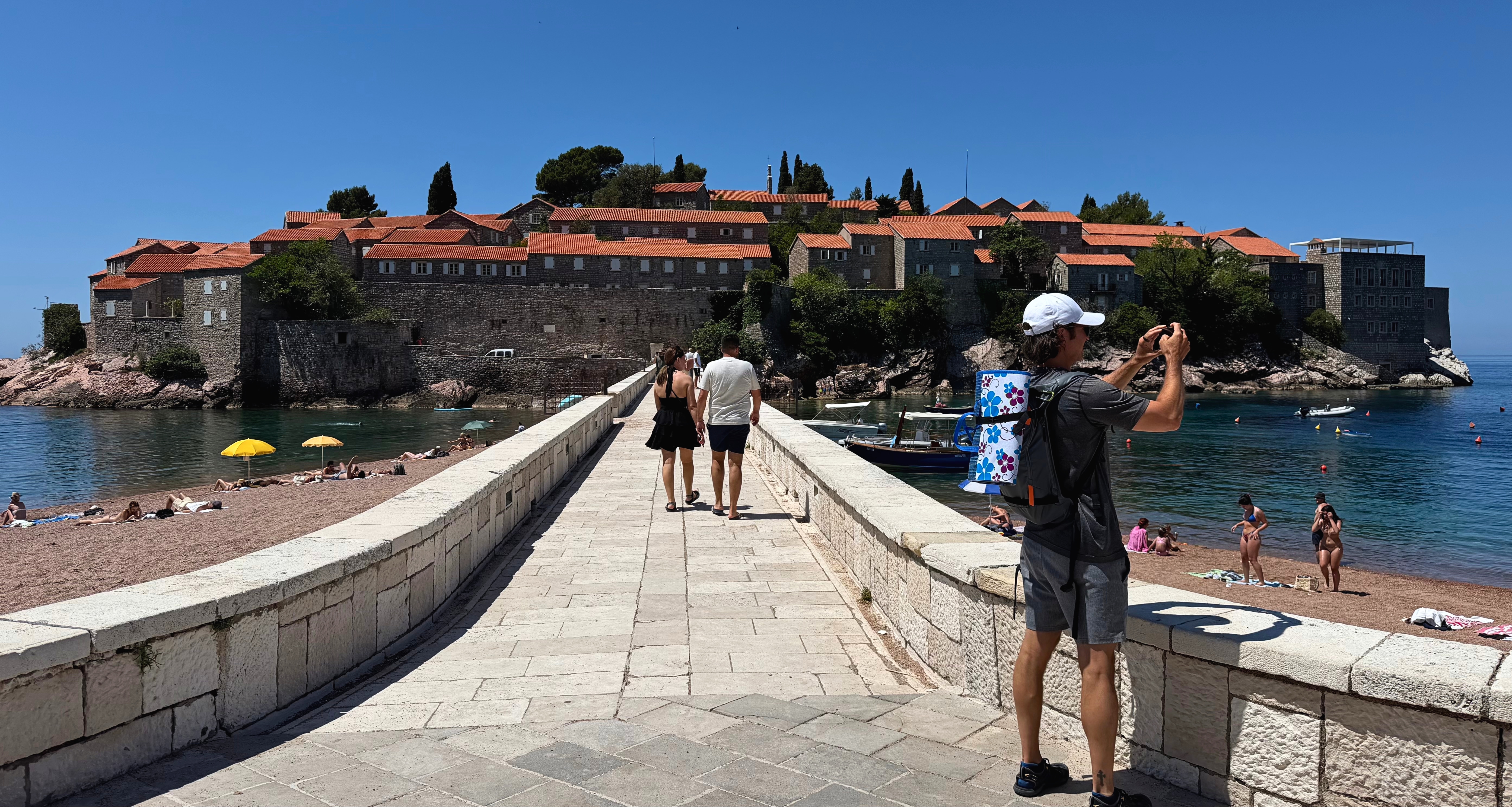 The causeway to Sveti Stefan, with beachgoers and the fortified island ahead.