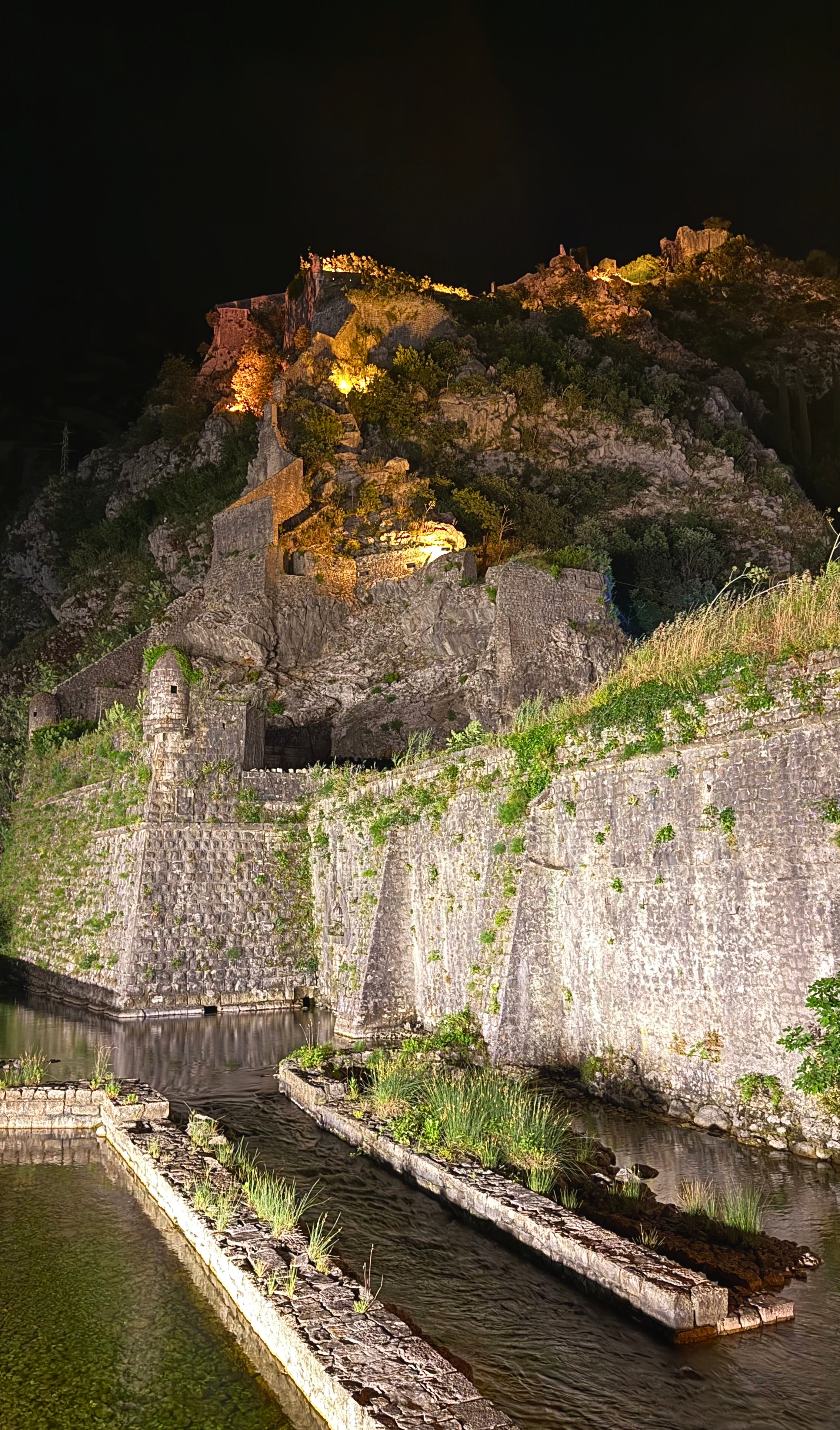 Kotor’s medieval fortifications lit after dark, climbing from the old city into the mountain above.