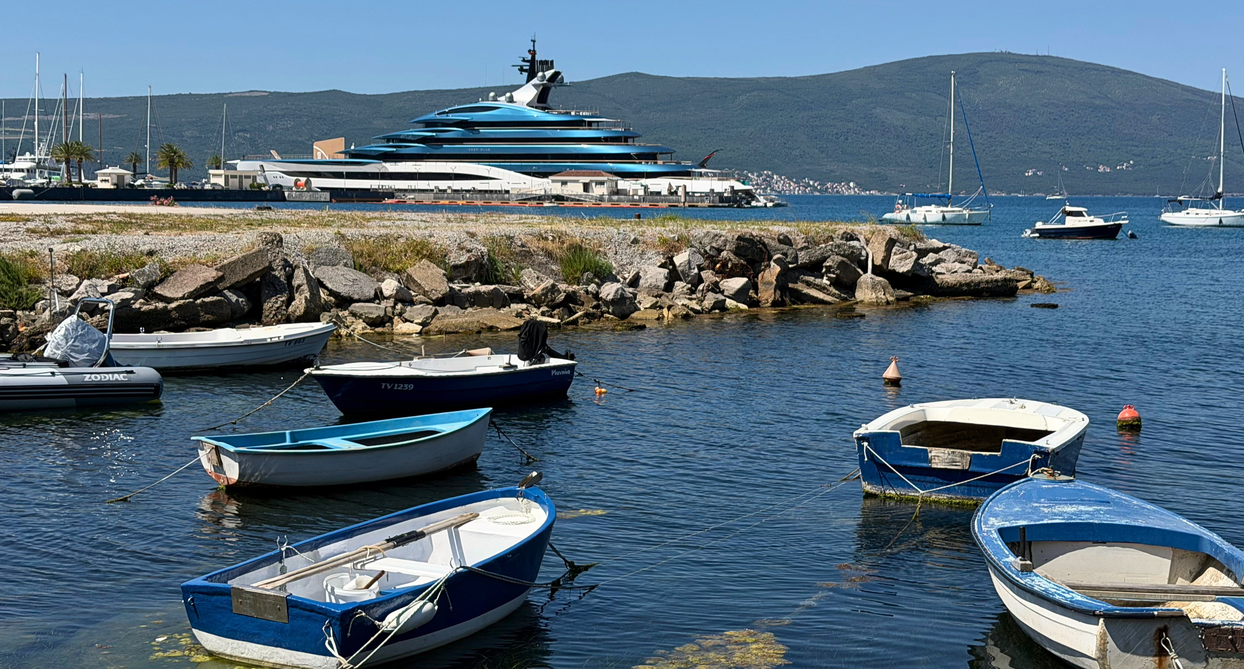 Tivat's waterfront, with small local boats in the foreground and superyachts beyond them