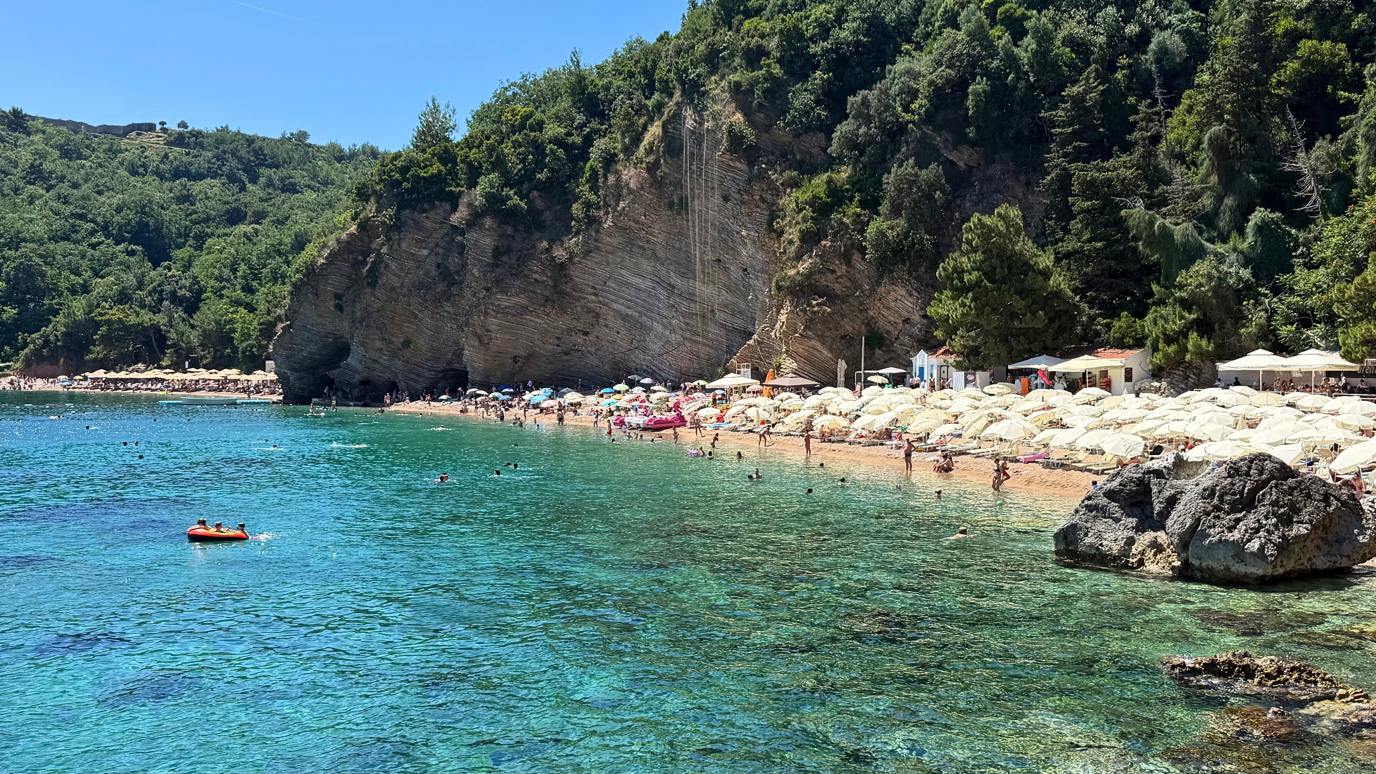 Mogren Beach, with clear water, limestone cliffs, and a busy summer shoreline along the coast