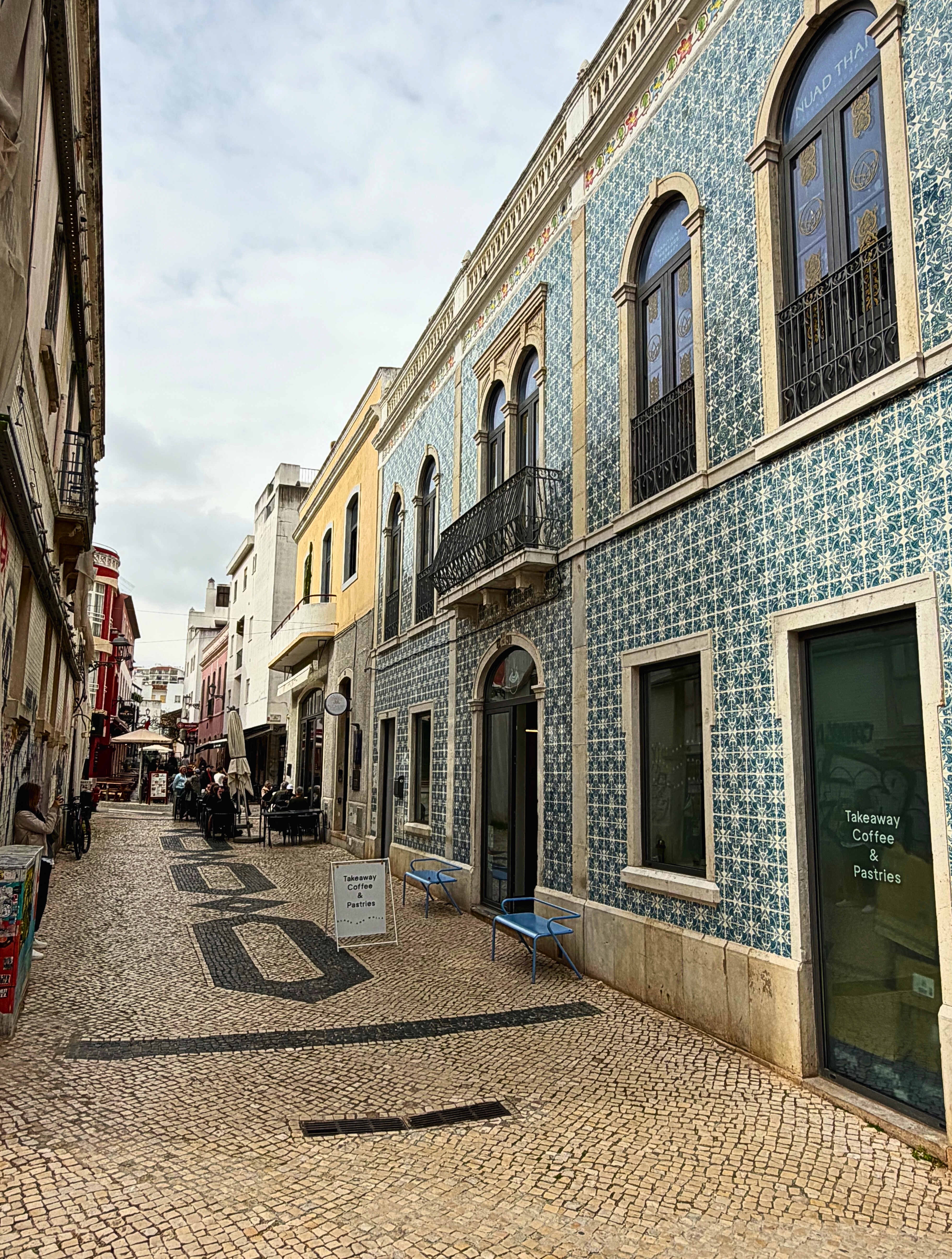 A tiled building and patterned calçada pavement on a narrow street in Lagos.