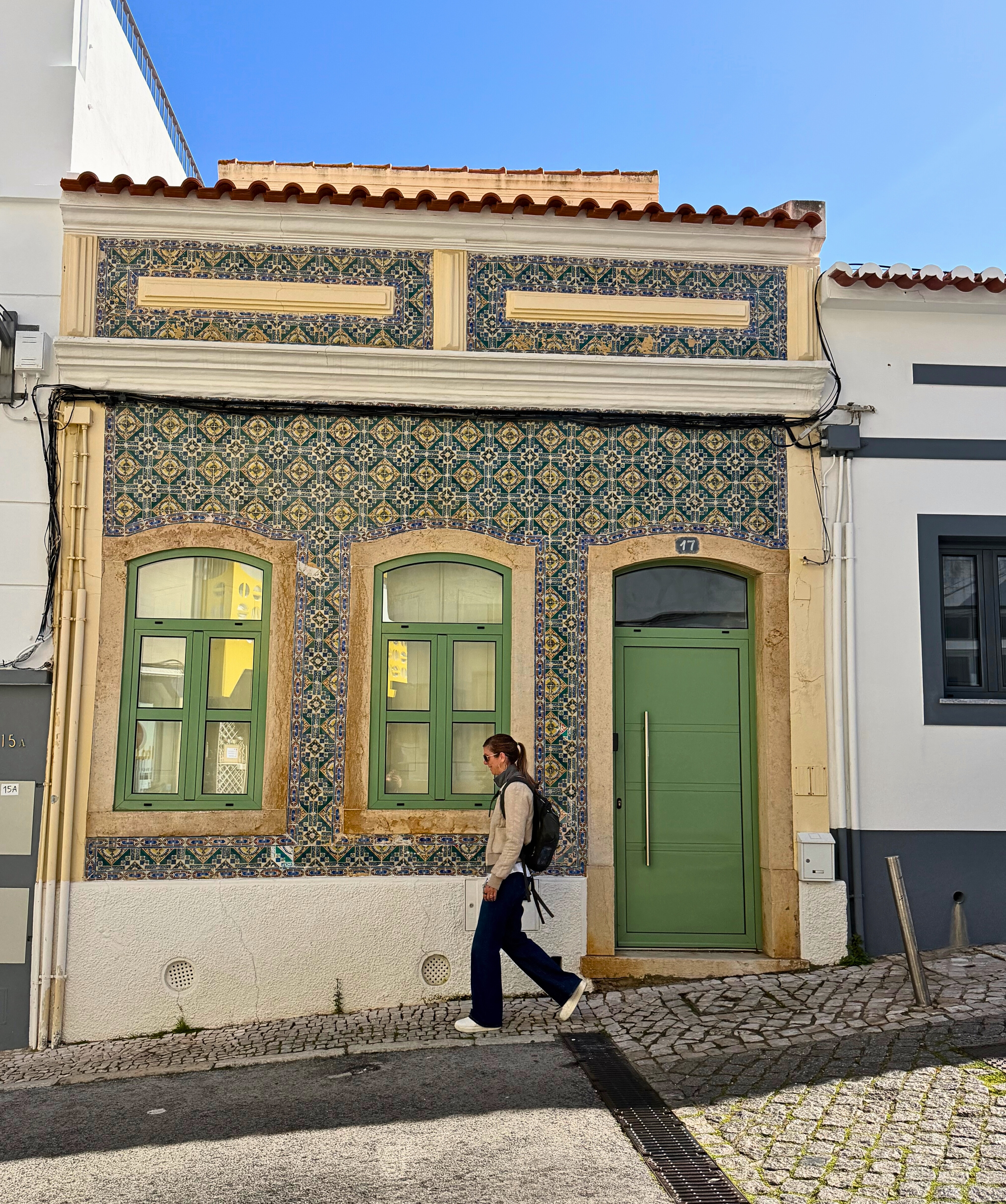 Stephanie walking past a tiled façade on a narrow Lagos street.