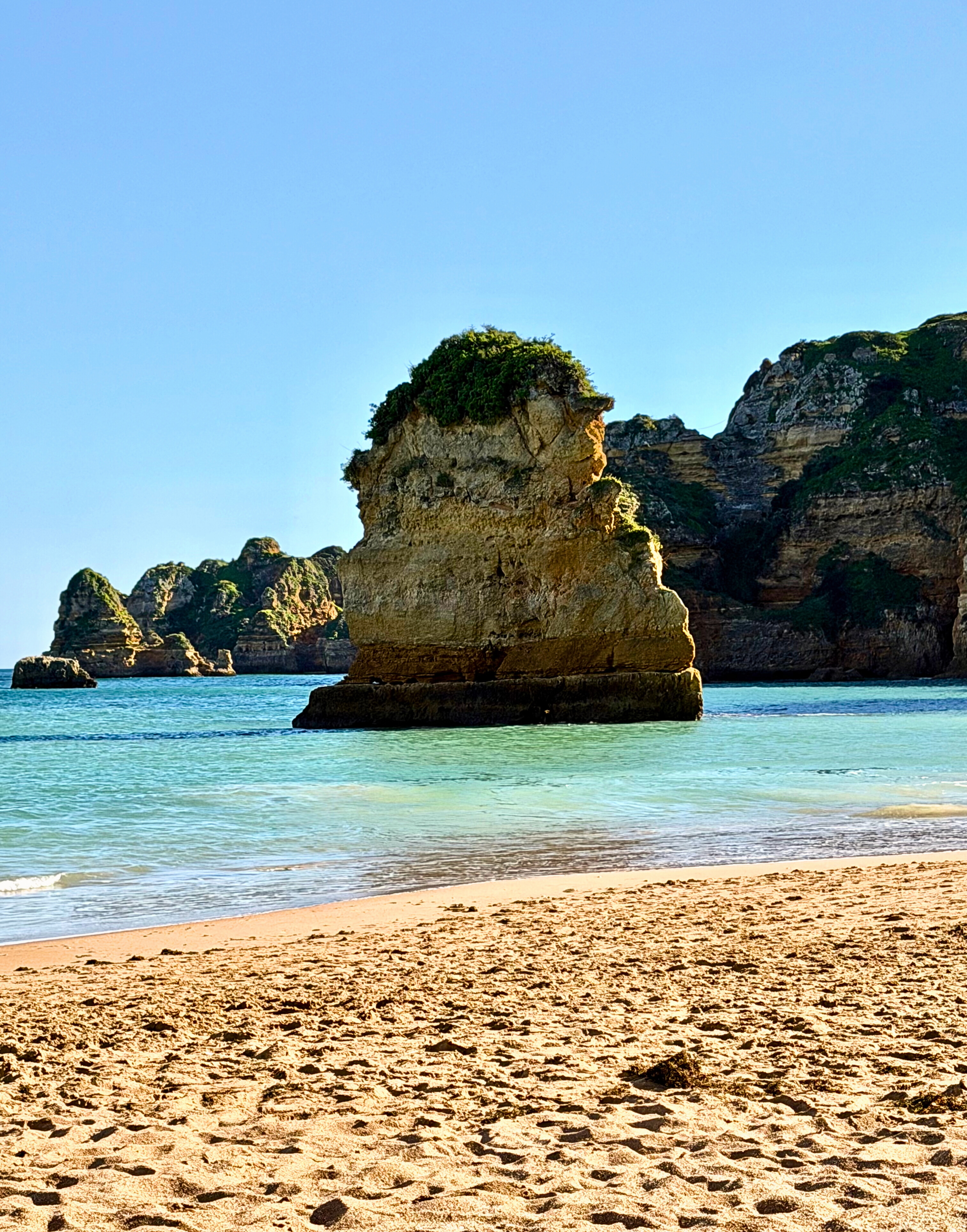 A beach-level view of sand, sea, and rock formations along the Algarve coast.