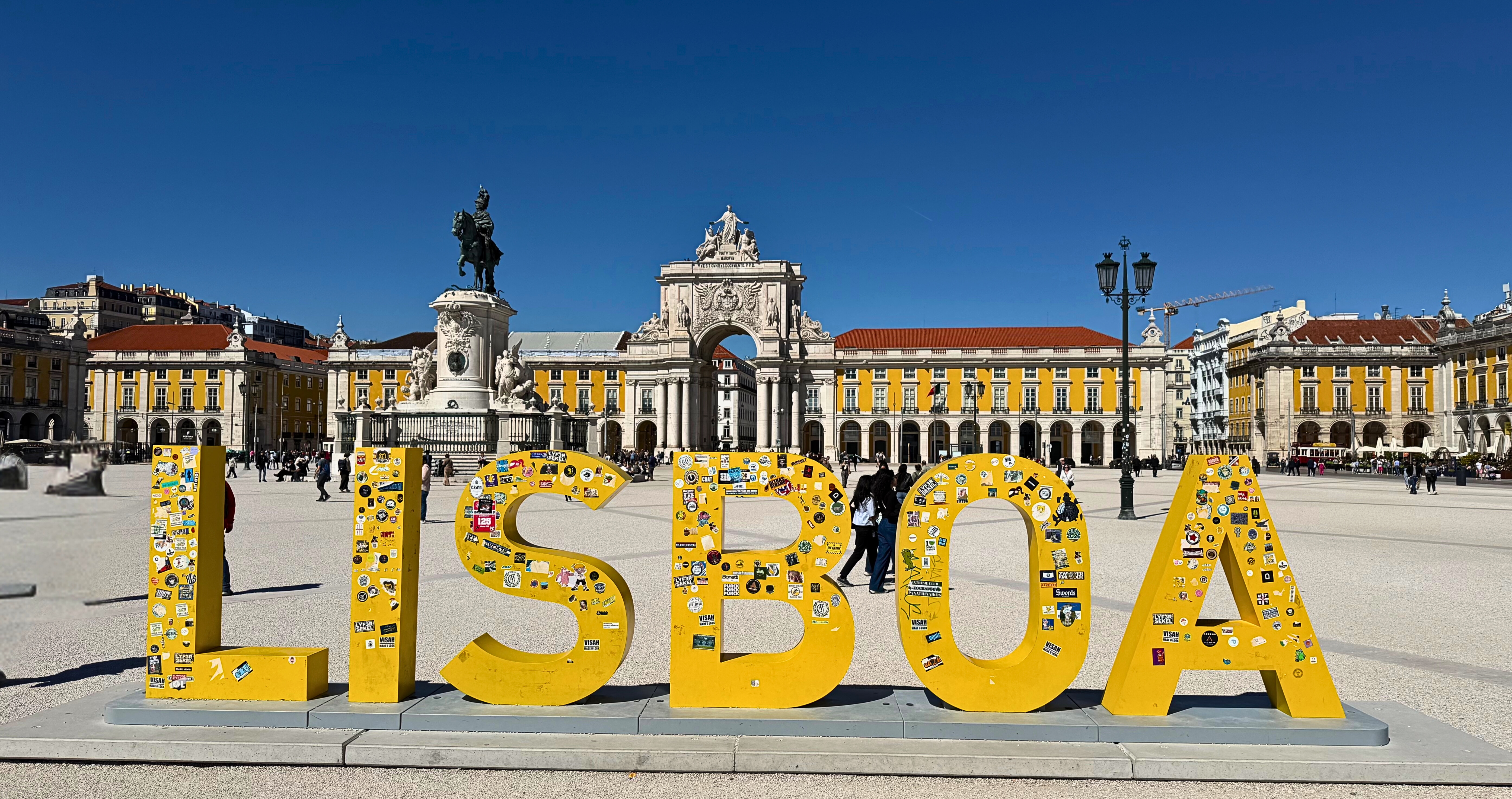 The yellow Lisboa sign in Praça do Comércio with the Arco da Rua Augusta behind it.