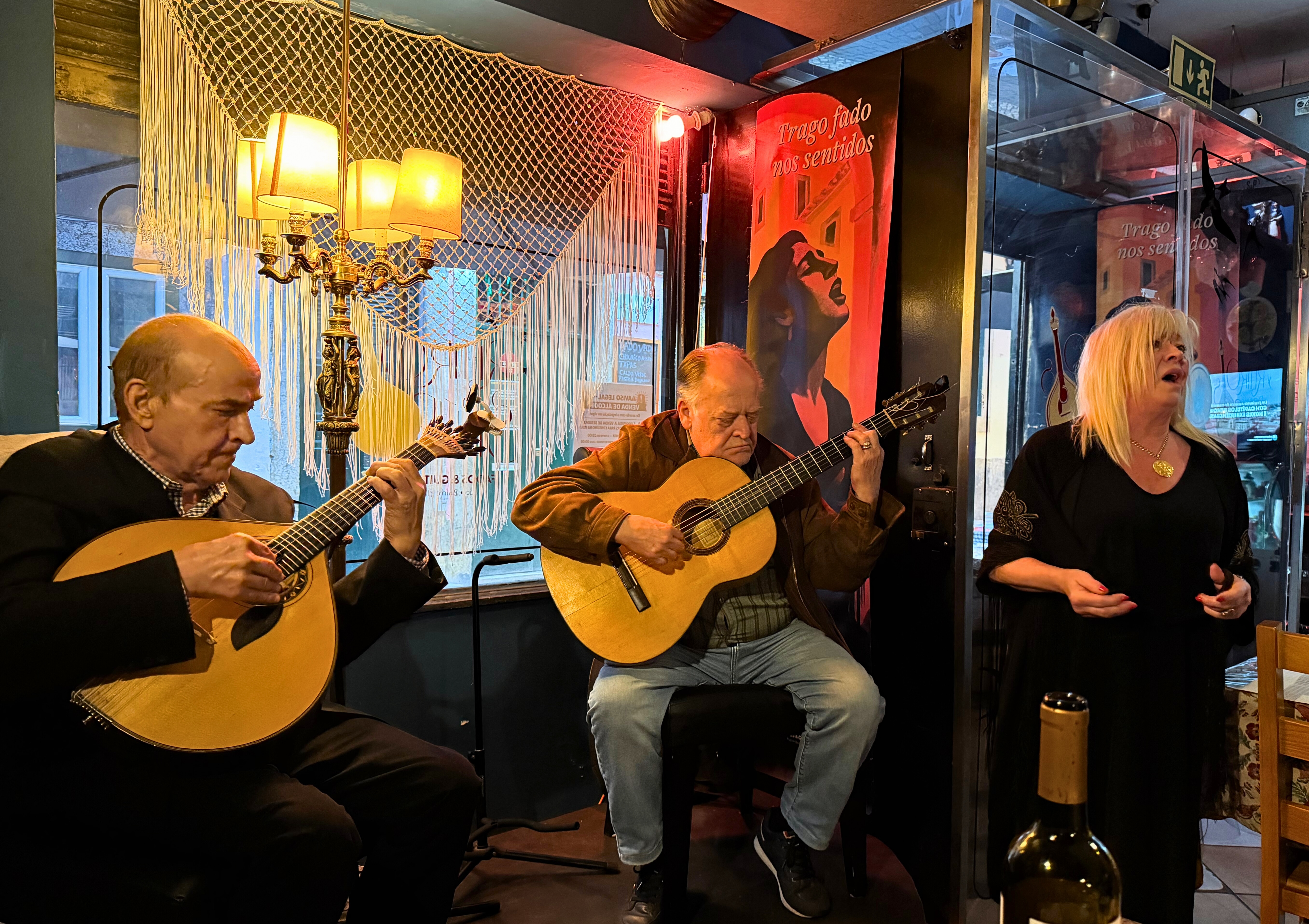 A Fado singer performing in a small Lisbon room with guitarists nearby.