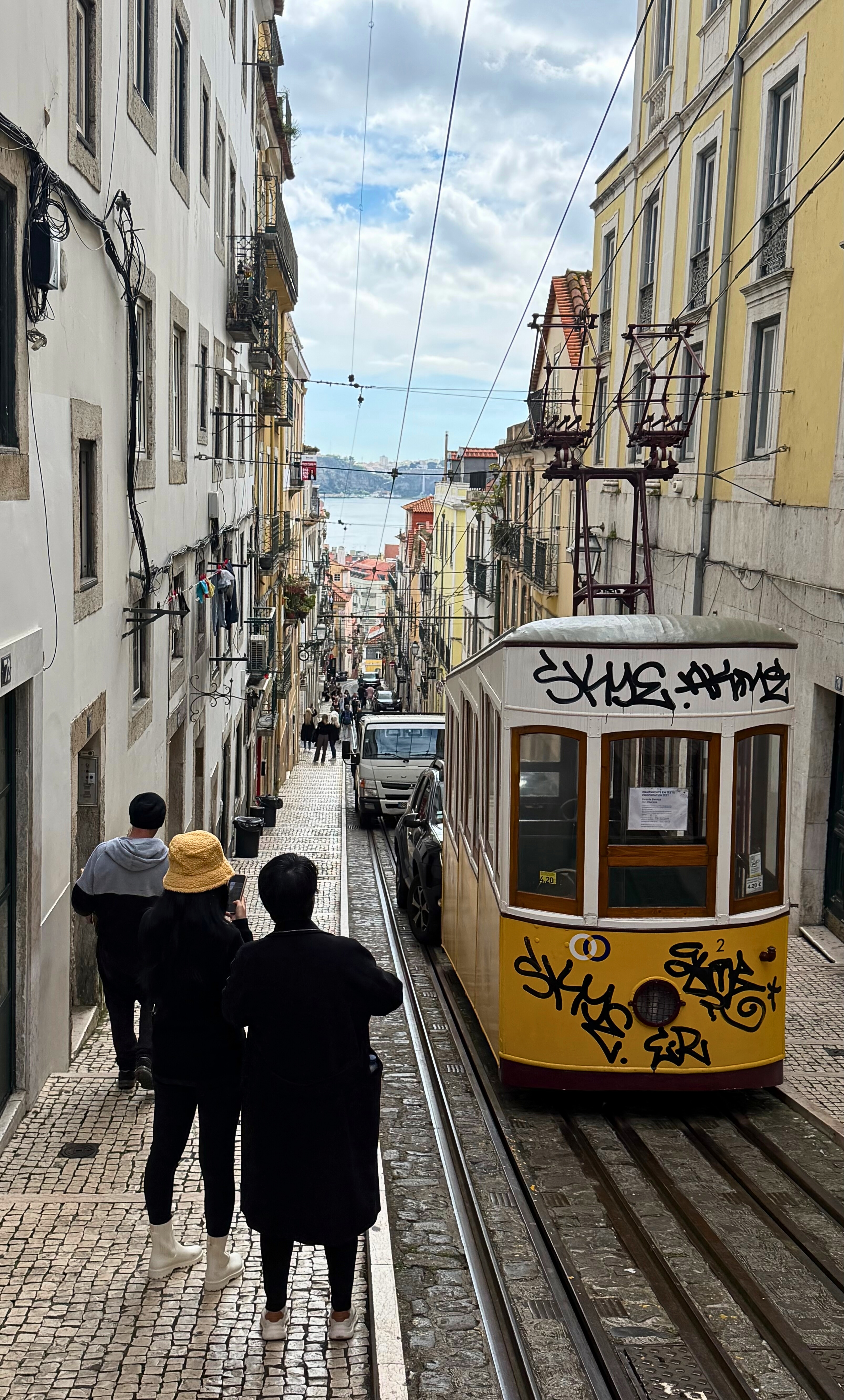A yellow tram moving through Lisbon streets.