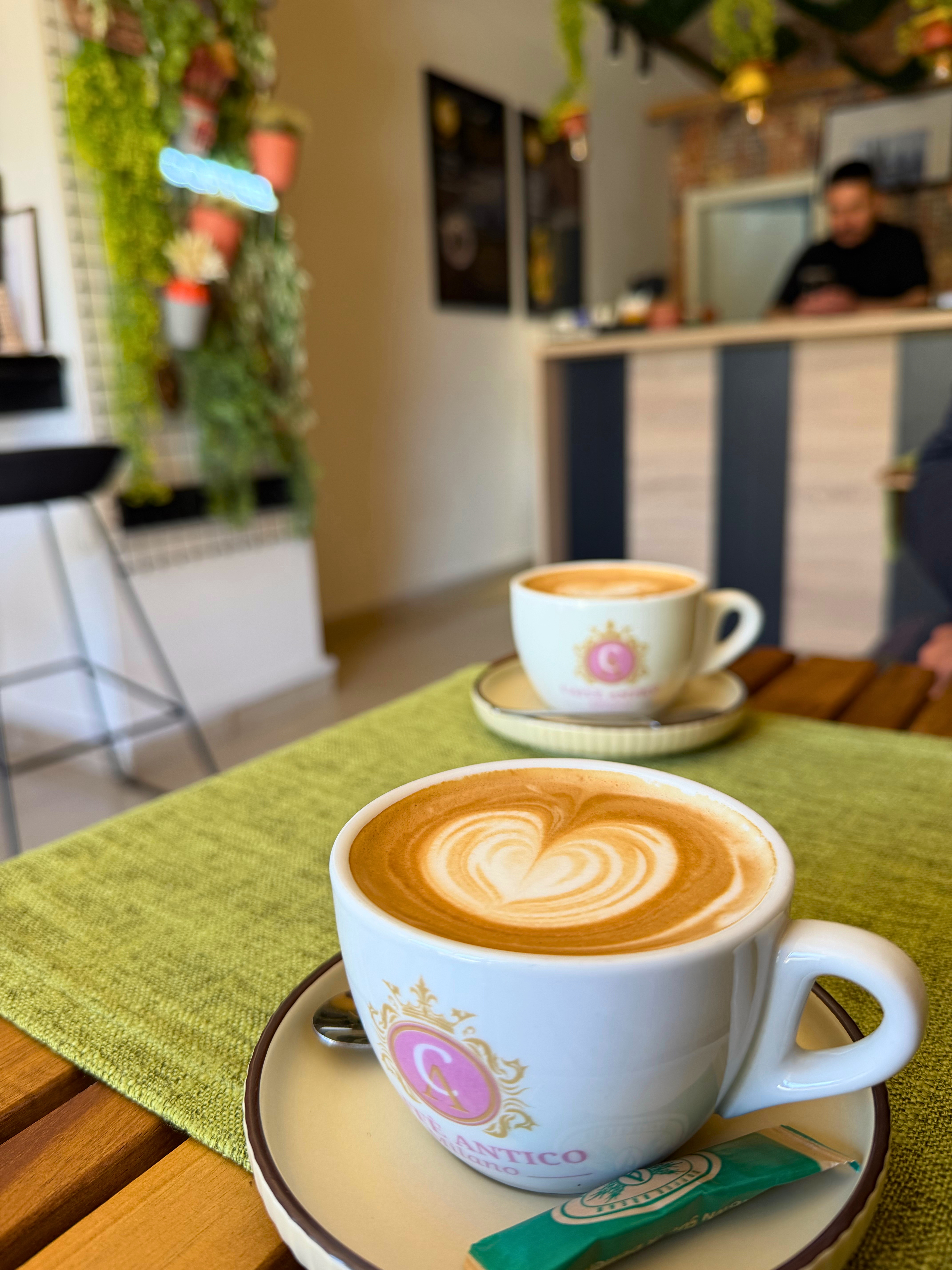 Two macchiatos on a table inside Kpyr coffee shop in Ohrid, with the counter and greenery in the background.