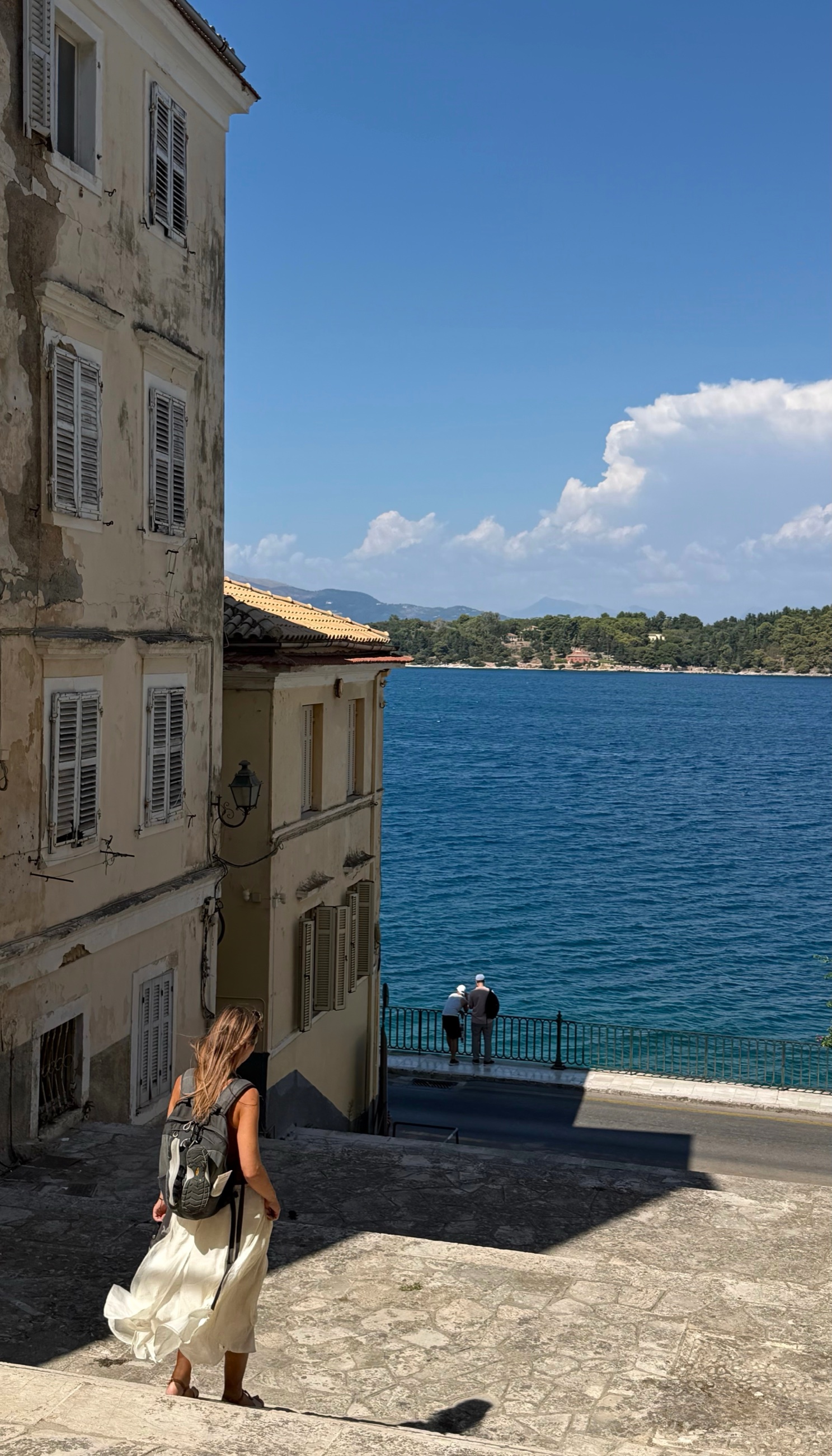 A downhill street in Corfu Town opening toward the blue Ionian Sea.