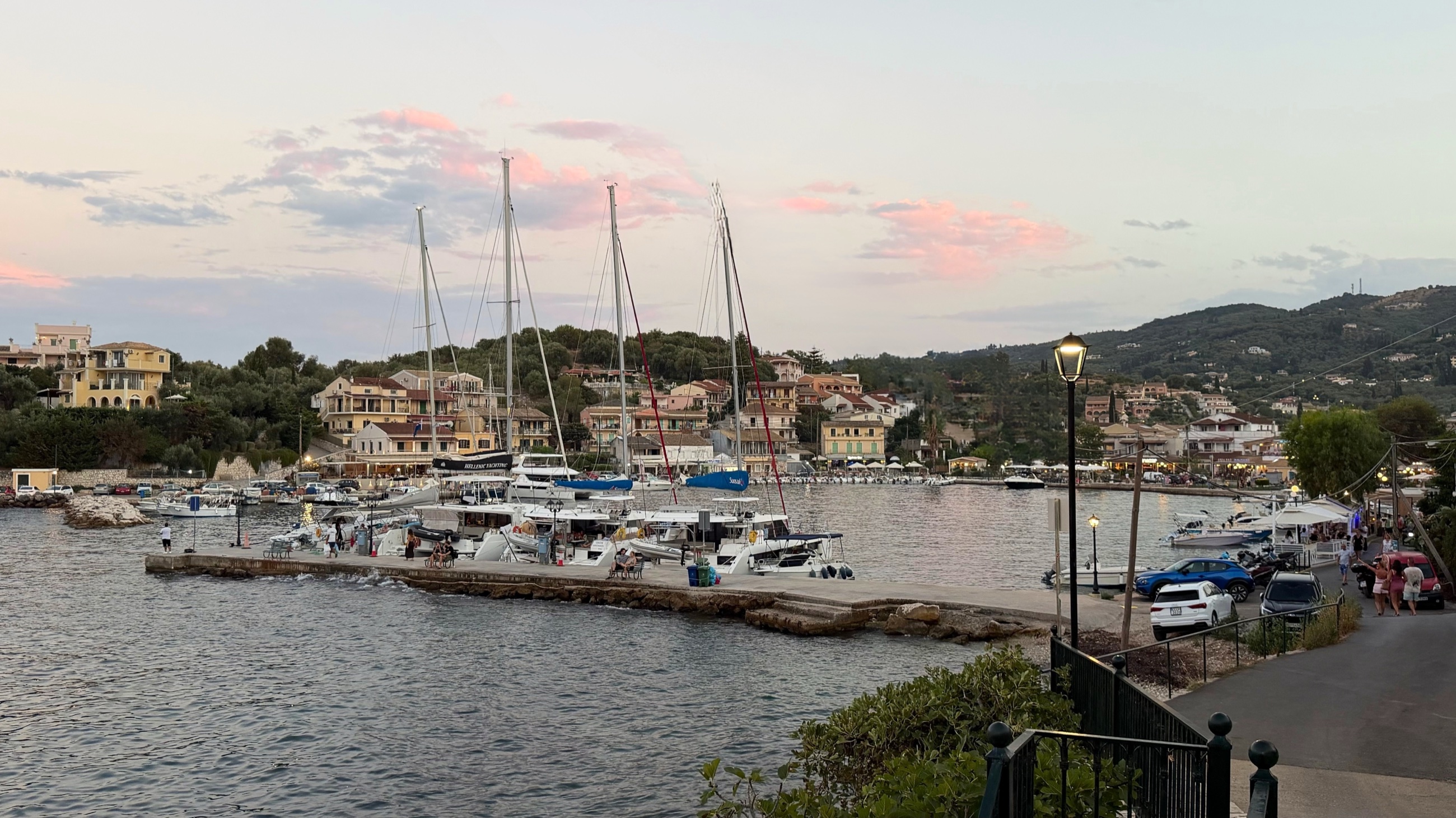 Kassiopi harbor at evening with sailboats and the village waterfront beyond.