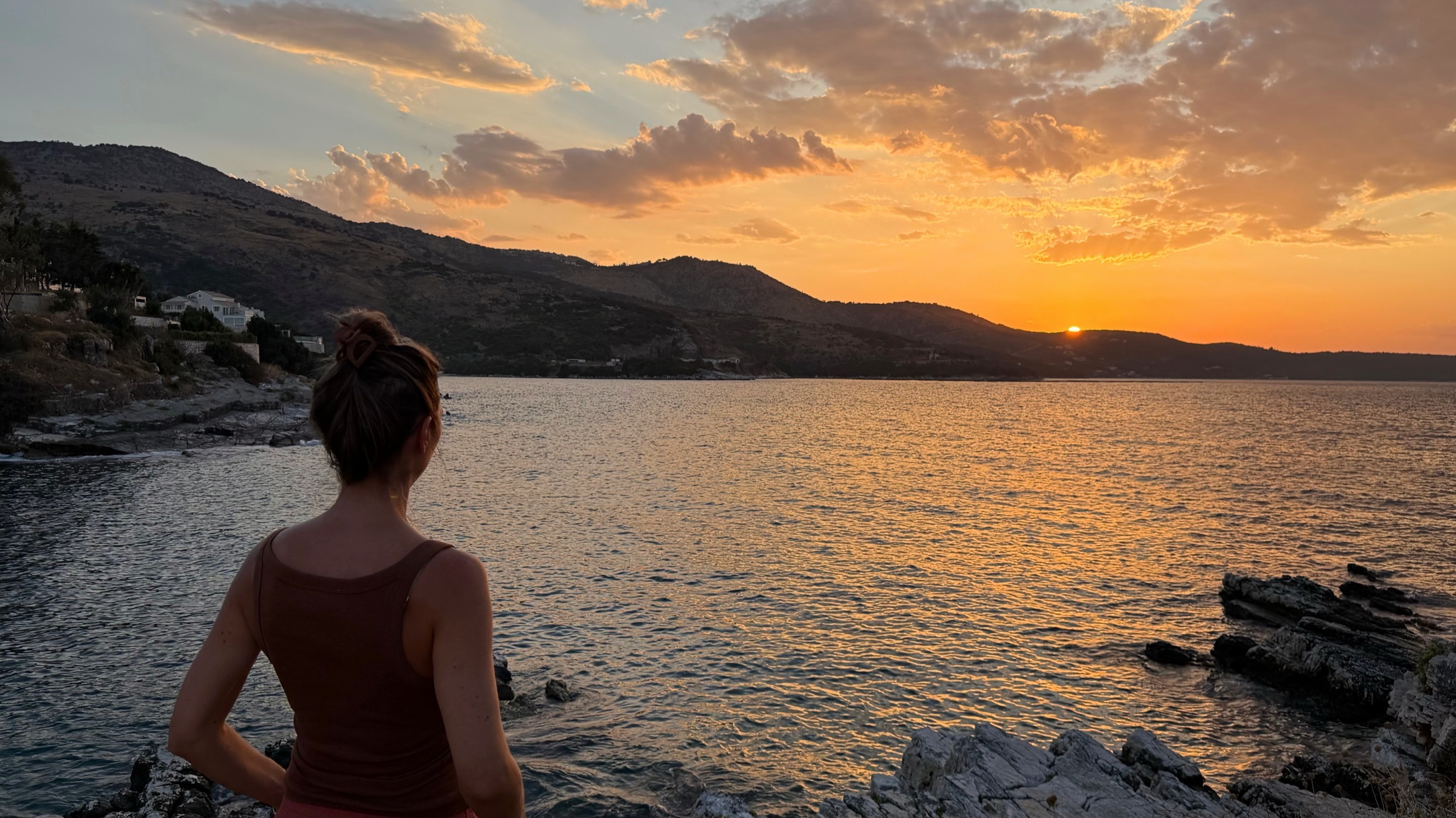 A woman looking toward the orange sunset over the water at Kassiopi.