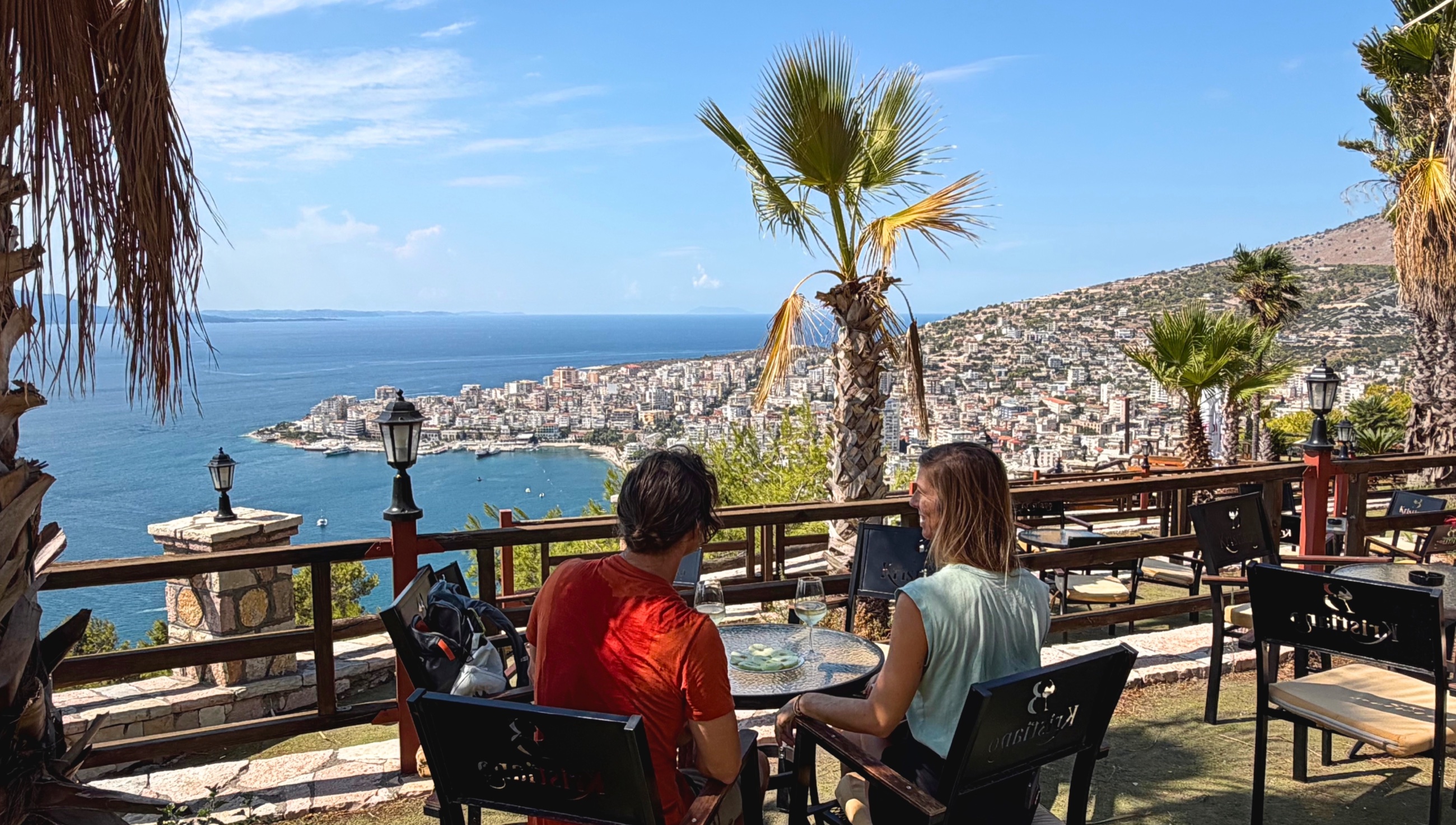 Two people seated on the terrace at Wine Bar Kristiano overlooking Sarandë and the Ionian Sea.