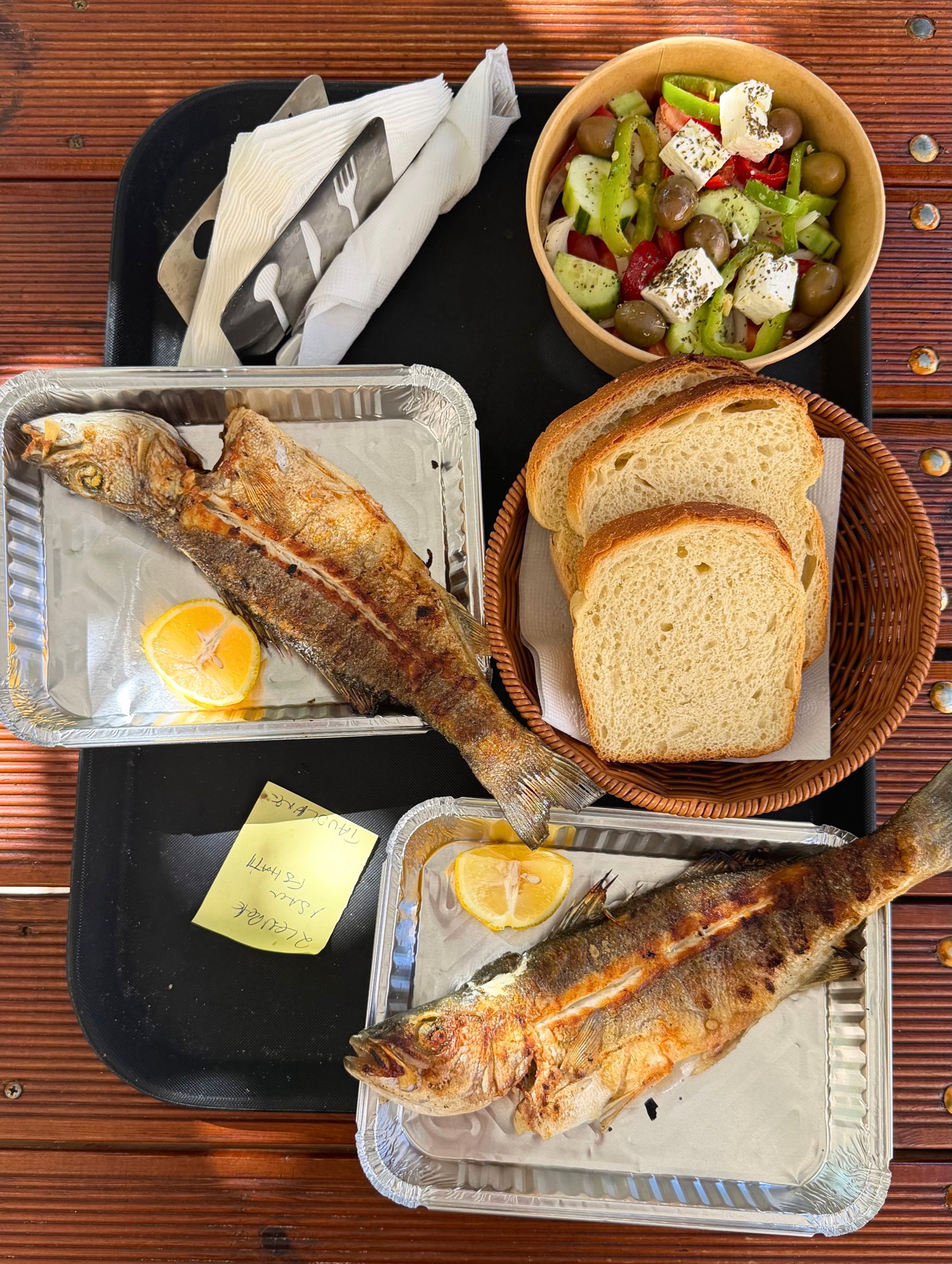 Whole grilled sea bass, village salad, and bread on a picnic table.