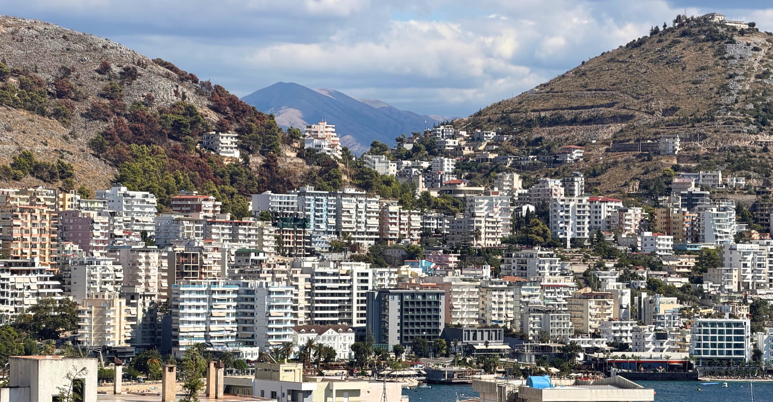 Dense apartment buildings rising into the dry hills above Sarandë.