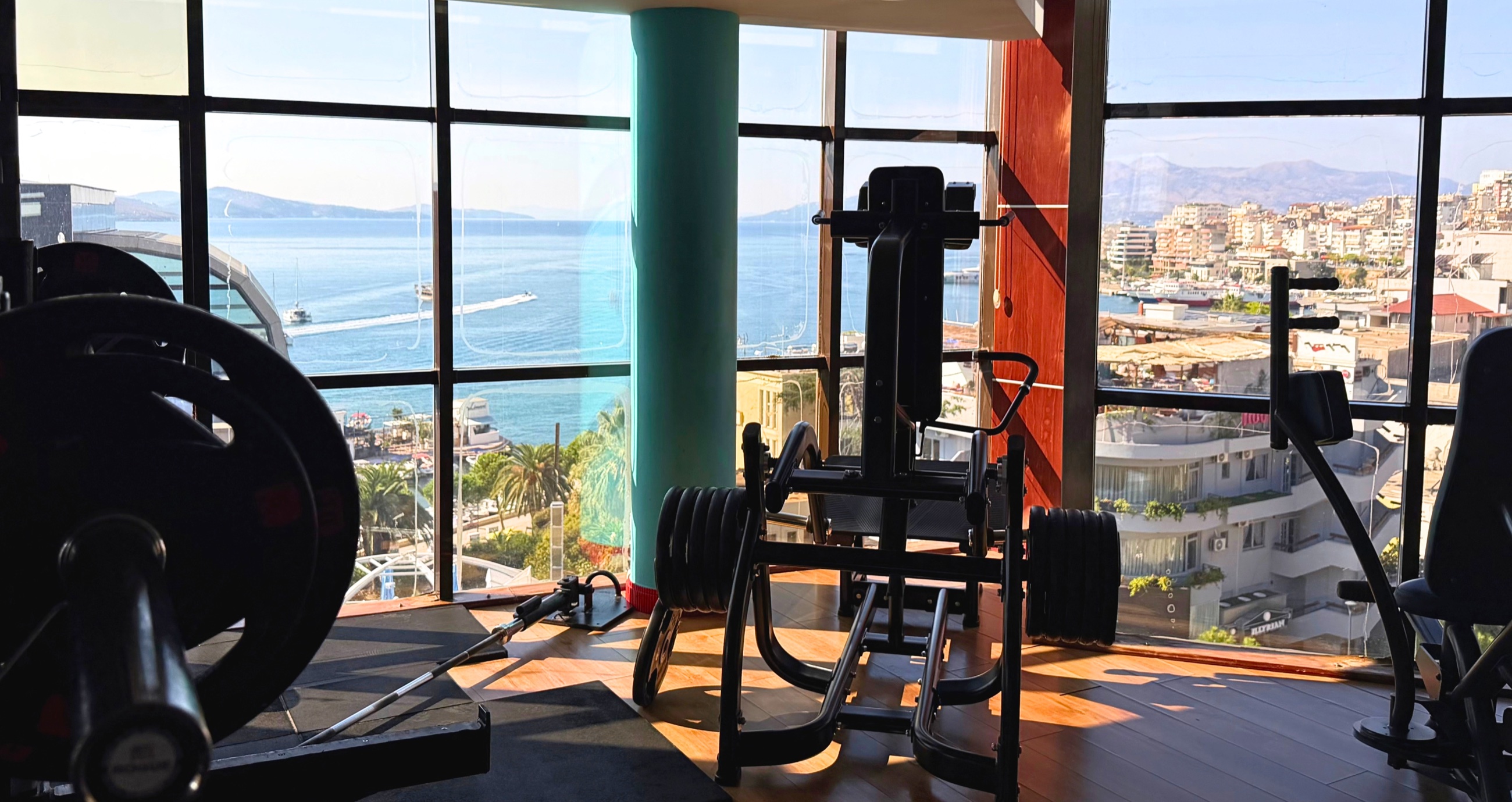 Gym equipment beside windows overlooking Sarandë Bay.