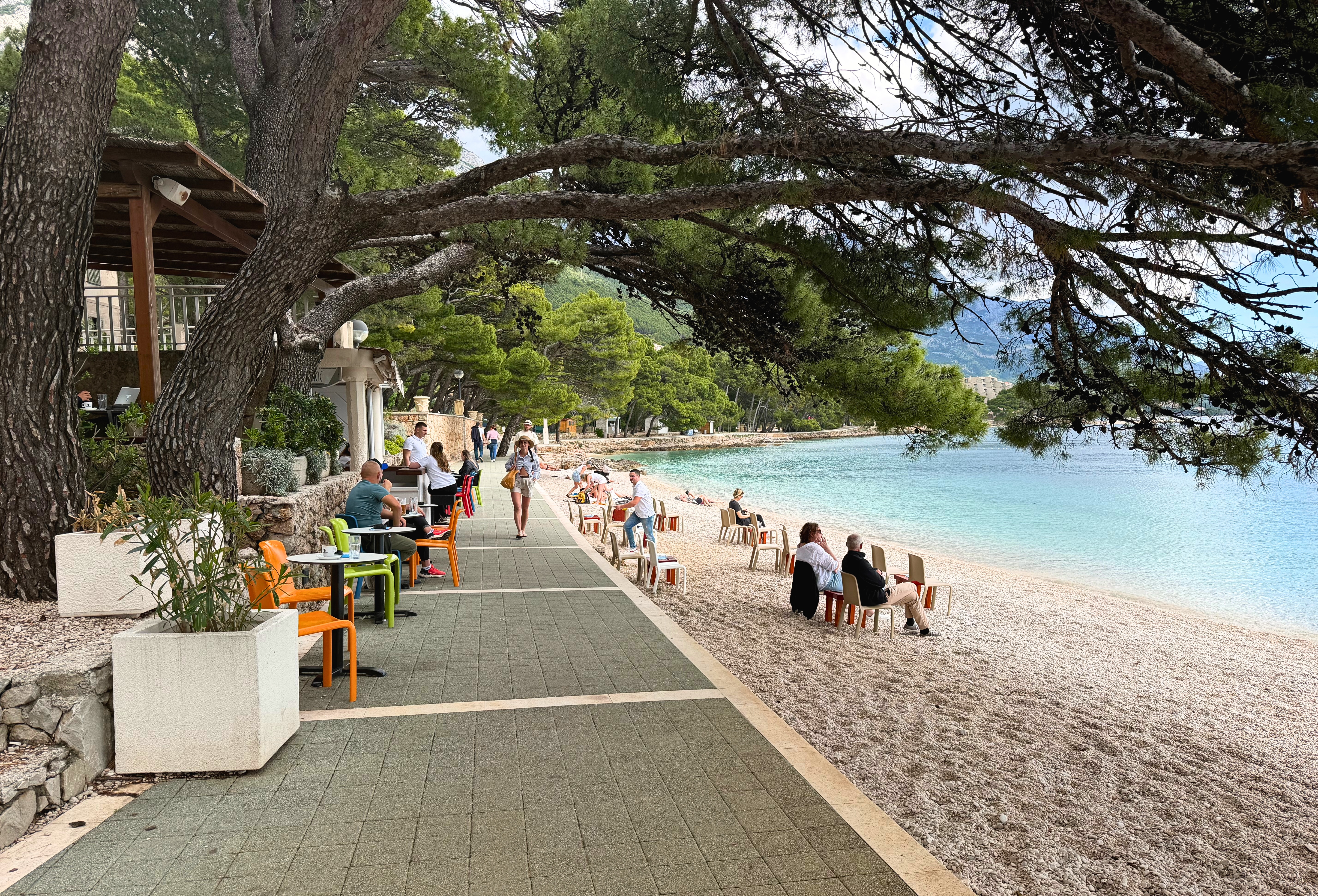 Brela coastal path with pine shade and café tables near the water