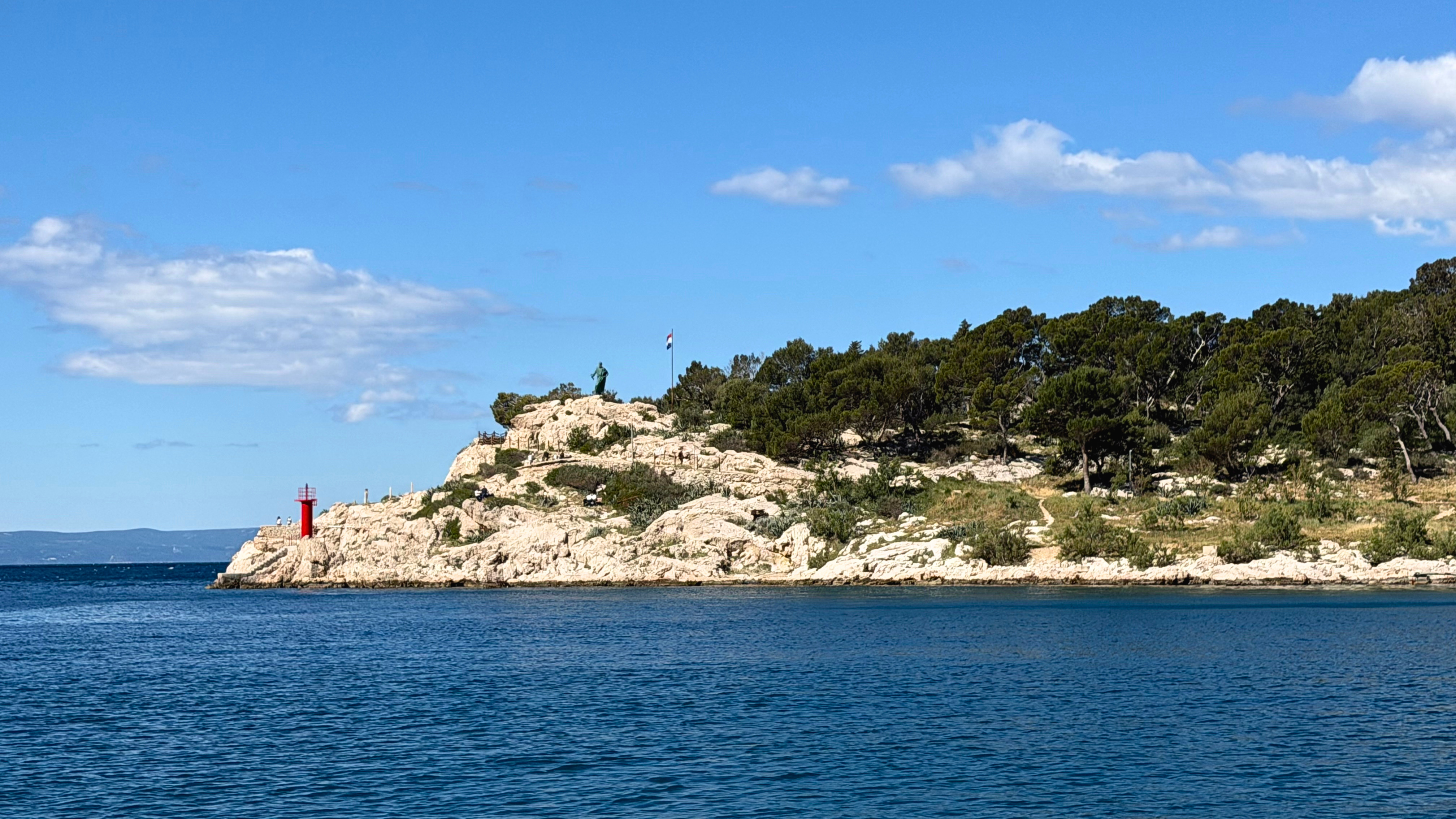 St. Peter Peninsula in Makarska with pine trees, harbor water, and the statue of St. Peter