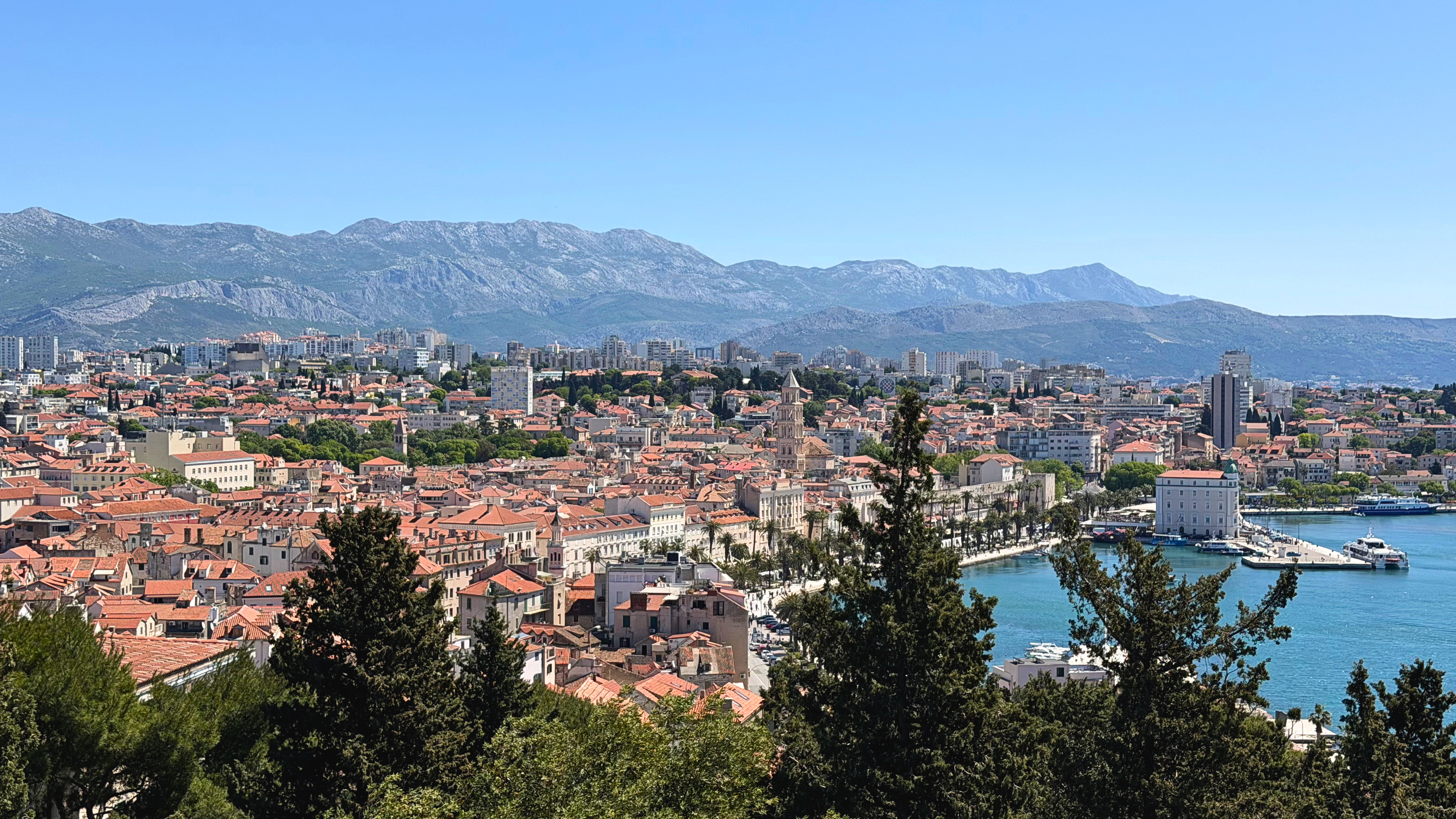 View of Split from Marjan Hill, with red rooftops, the Adriatic Sea, mountains, and the old city below.
