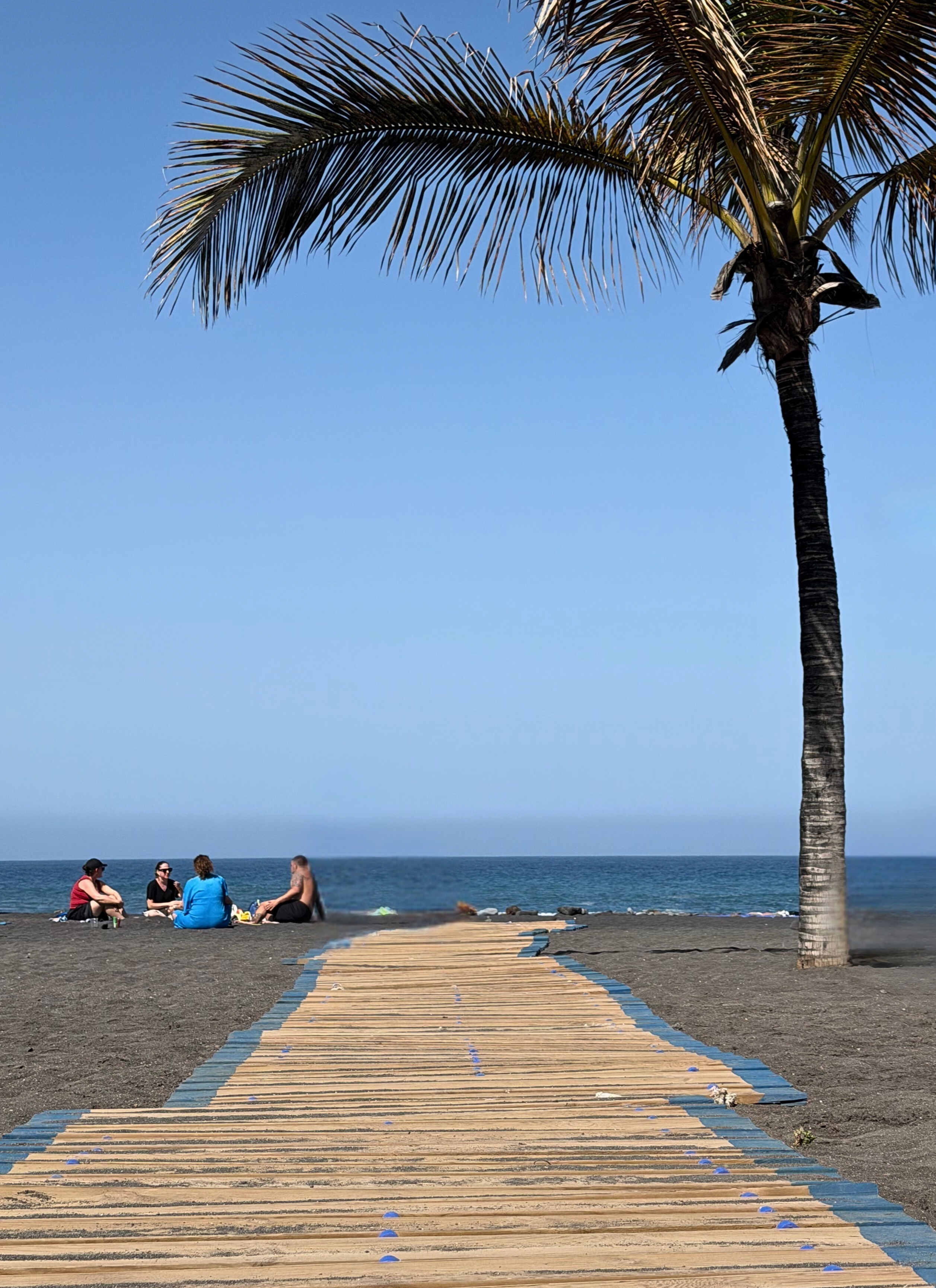 A wooden walkway leading across black sand at Playa Jardín in Puerto de la Cruz.