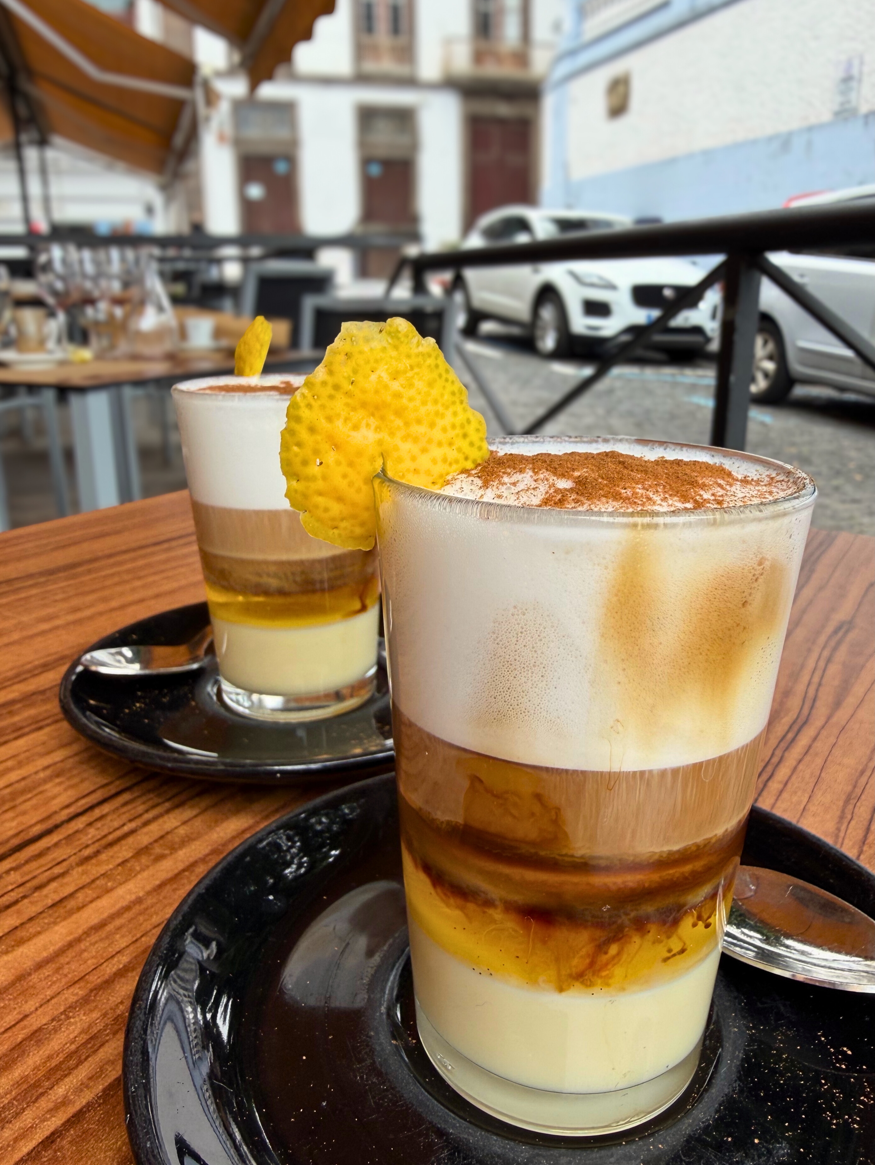 Two barraquito coffees with layered milk, coffee, foam, and lemon peel.