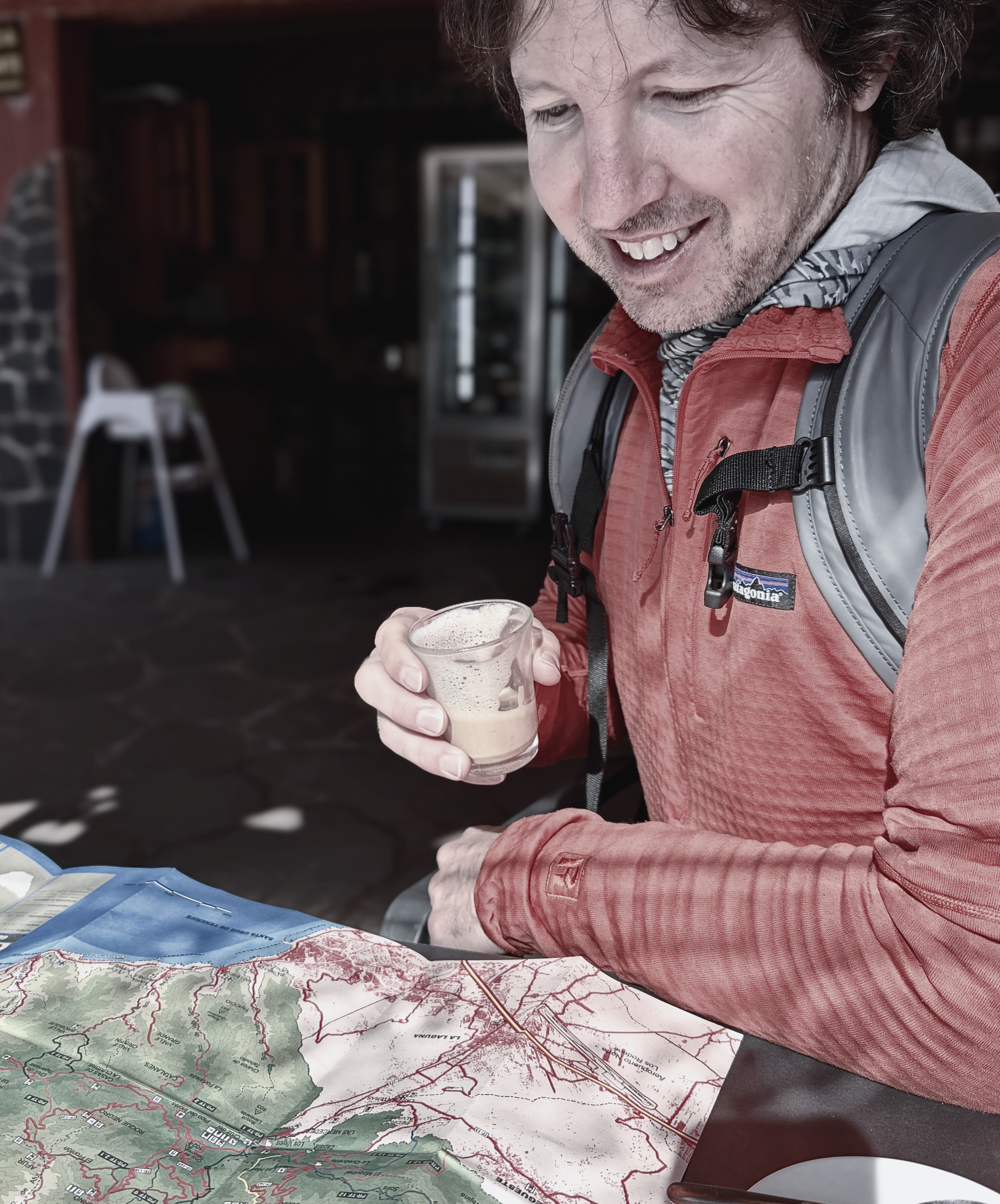Sam sits at a café table with a cortado and a trail map before a Tenerife hike.