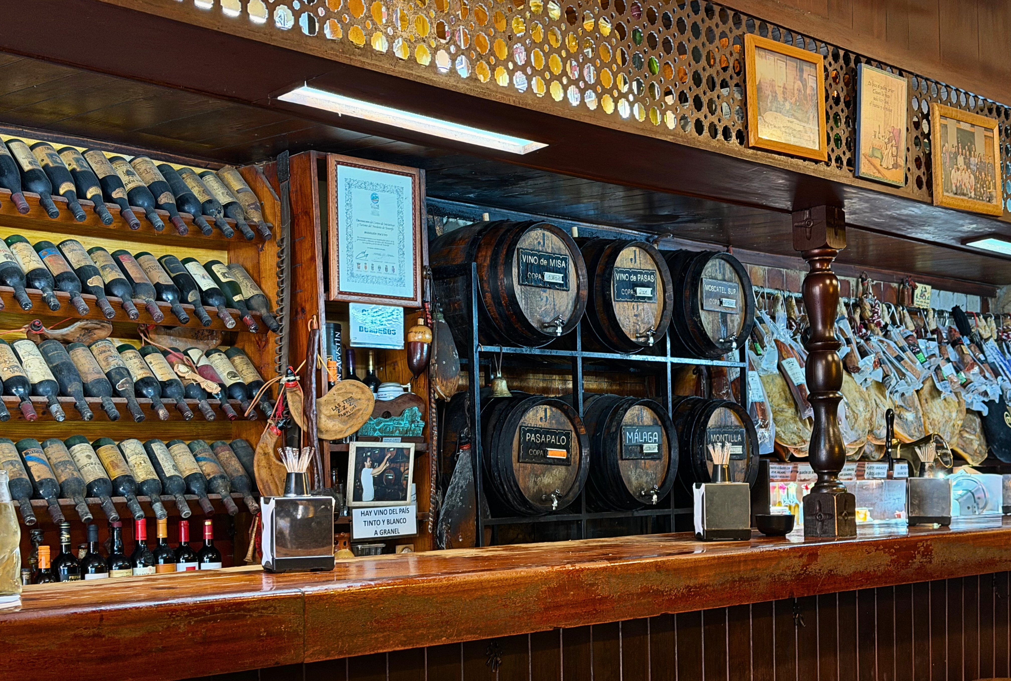 The interior of a Spanish tasca with barrels on the wall and jamón overhead.