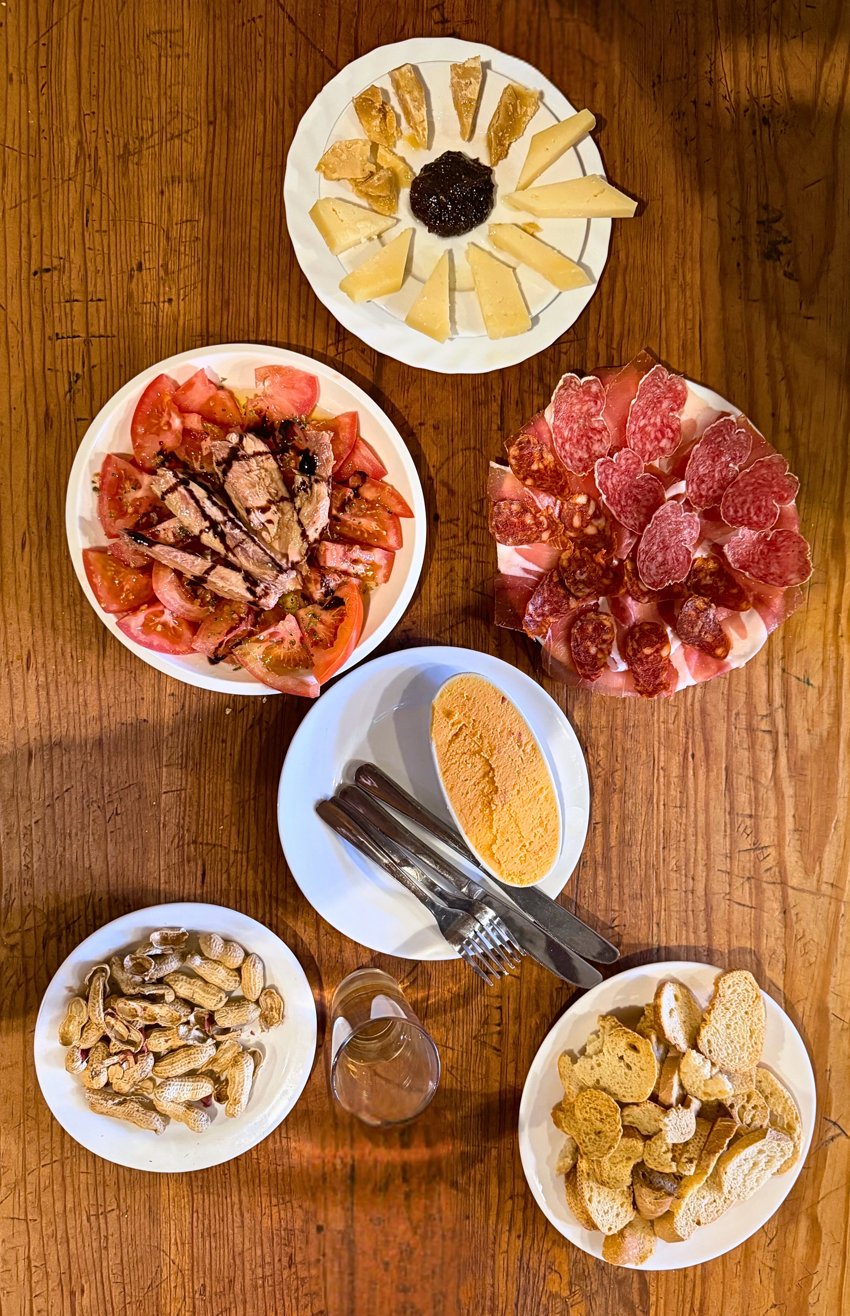 A table of cold tapas with cheese, tomatoes, tuna, cured meats, bread, and dip.