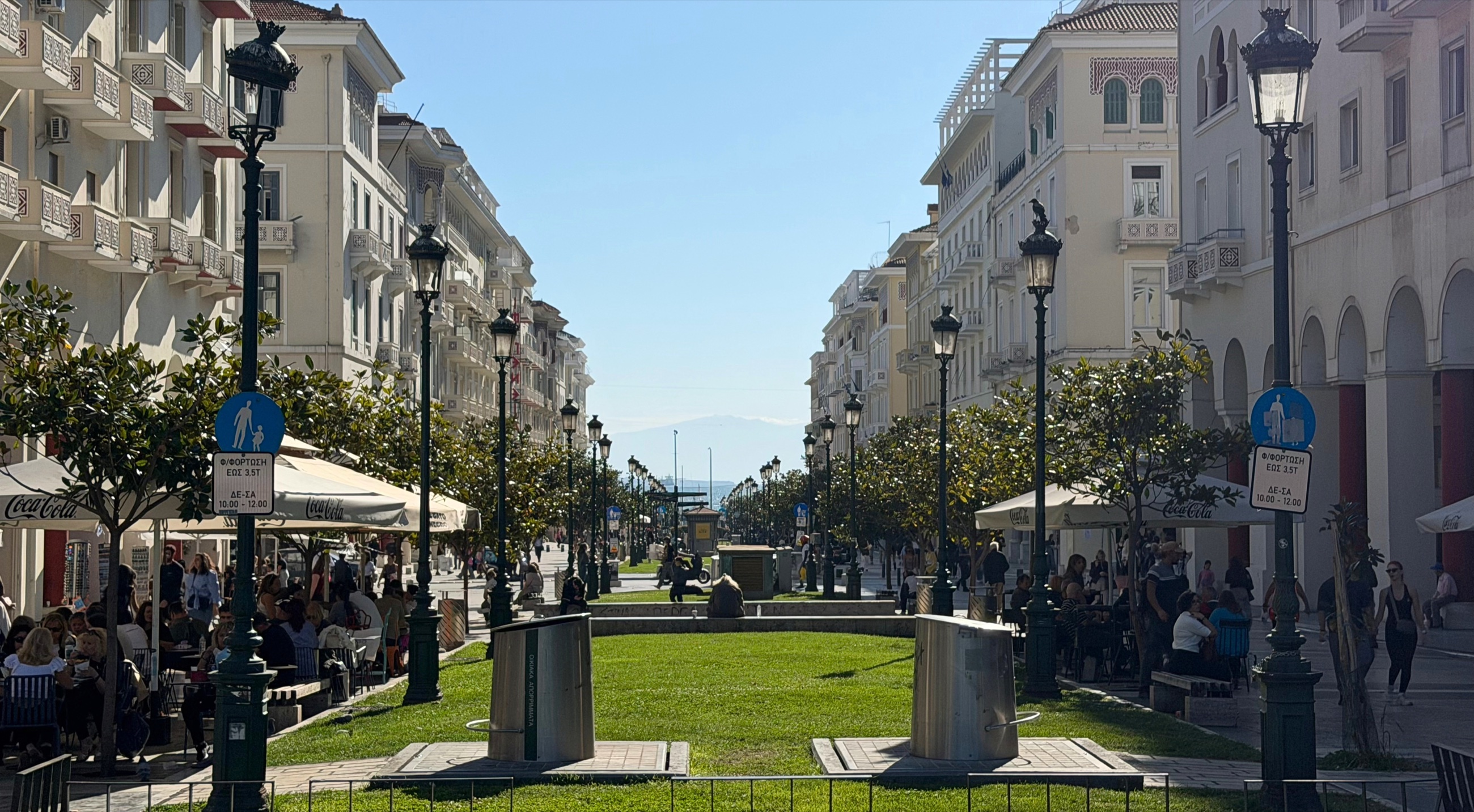 A tree-lined pedestrian street leading toward Aristotelous Square and the sea