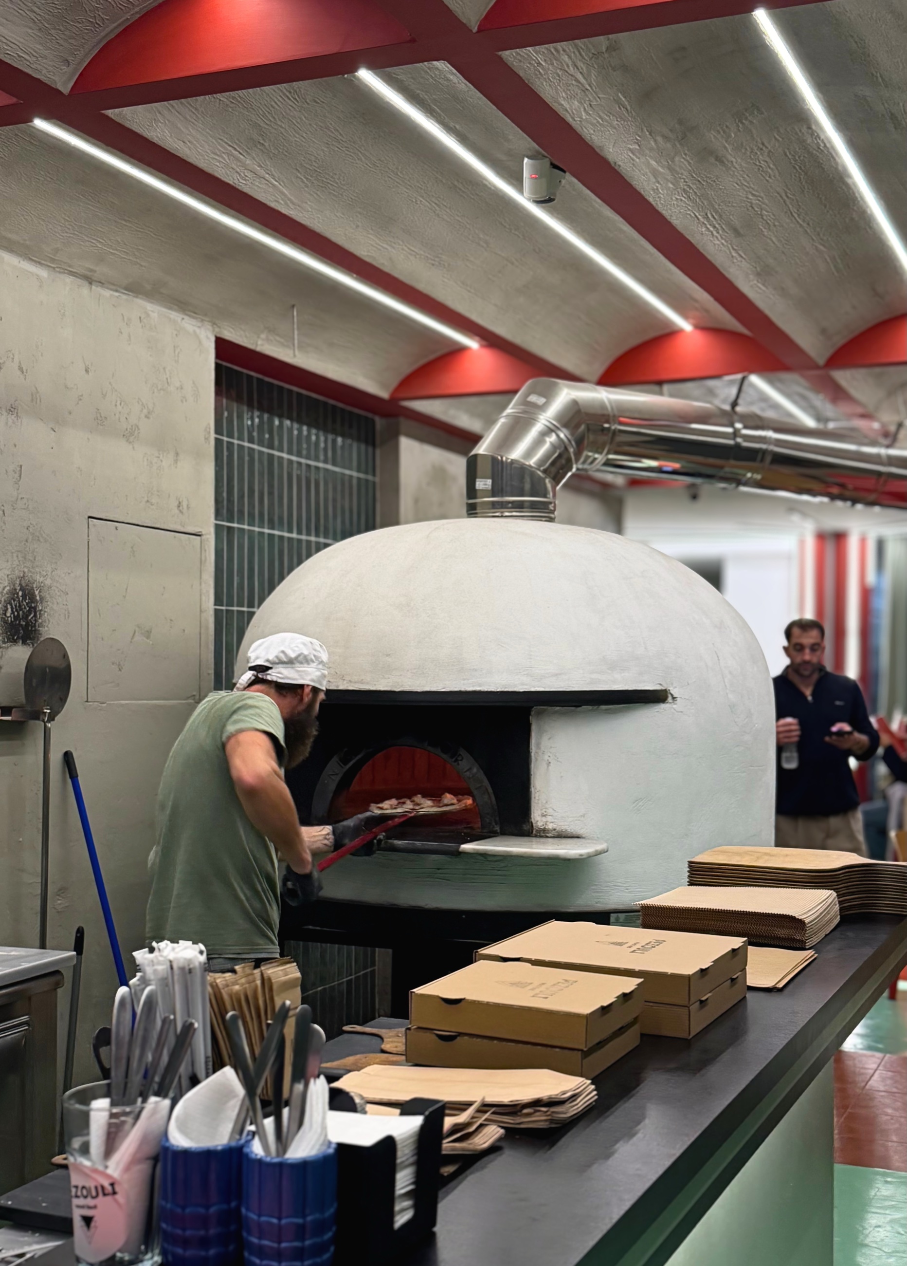 Pizza maker pulling a pizza from a wood-fired oven in Thessaloniki