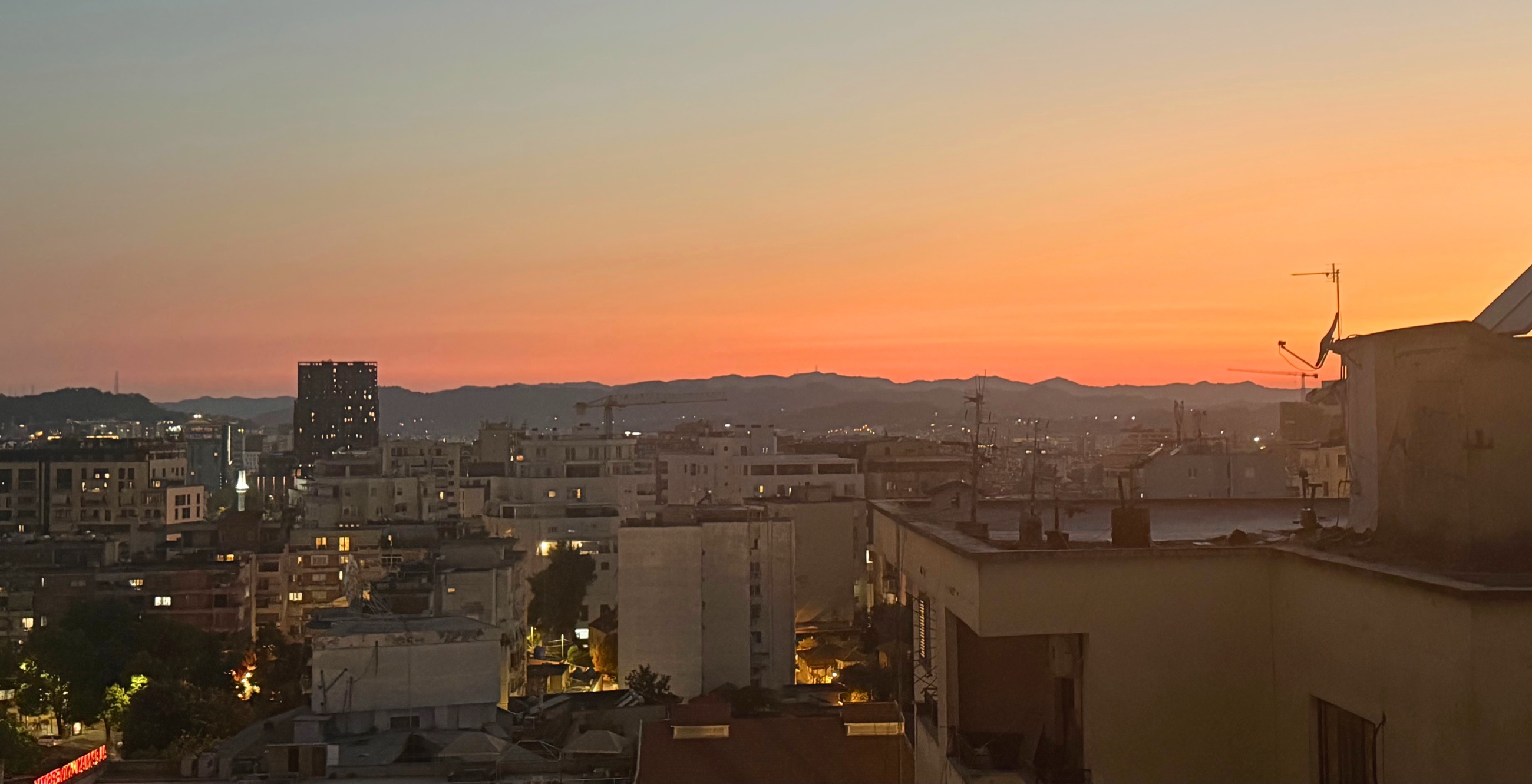 Sunset over Tirana with the city skyline and surrounding mountains in warm evening light.
