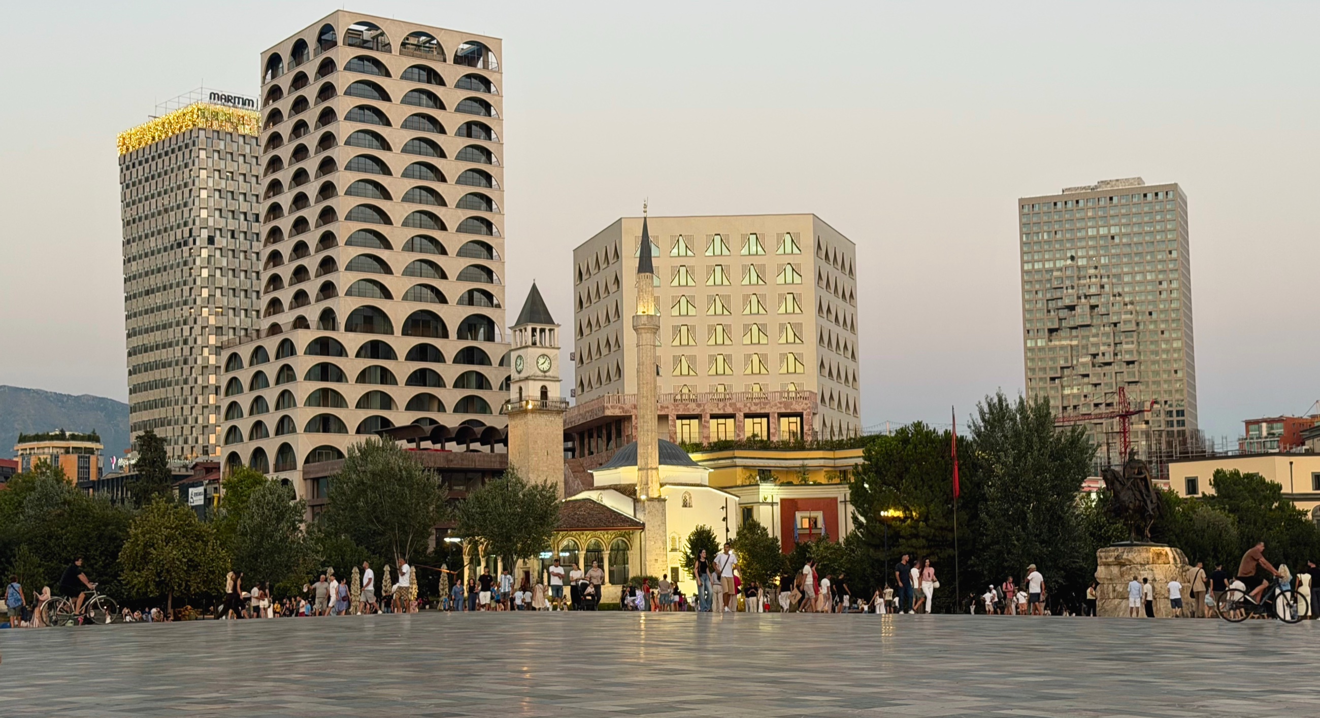 Skanderbeg Square in Tirana at dusk, with the Et'hem Bey Mosque, clock tower, and modern buildings surrounding the plaza.