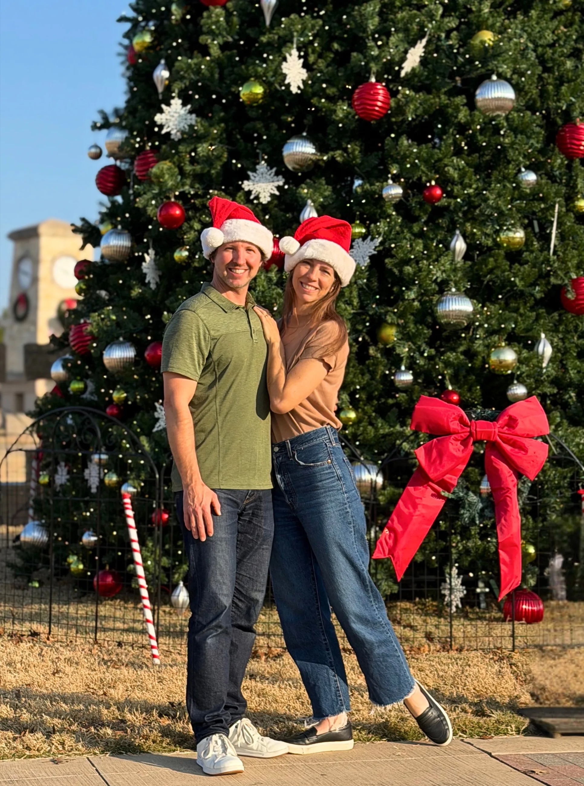 Sam and Stephanie in Santa hats in front of a decorated Christmas tree in Dallas.