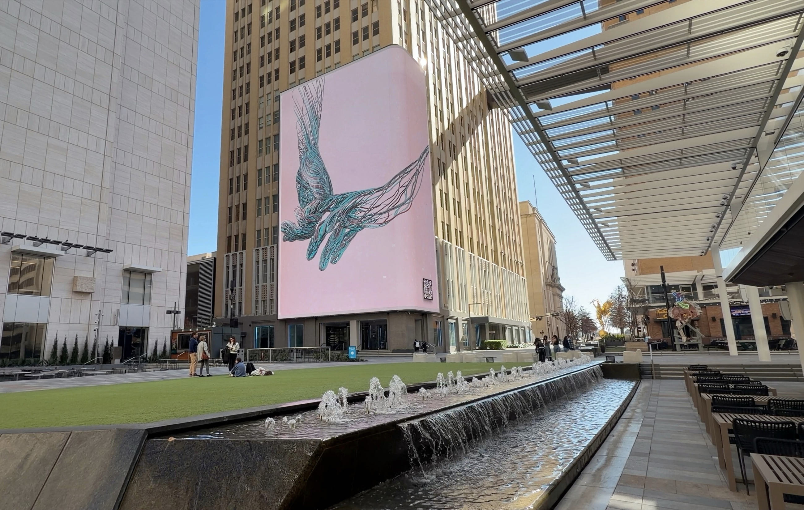 People walking near water features and large screens at AT&T Discovery District.