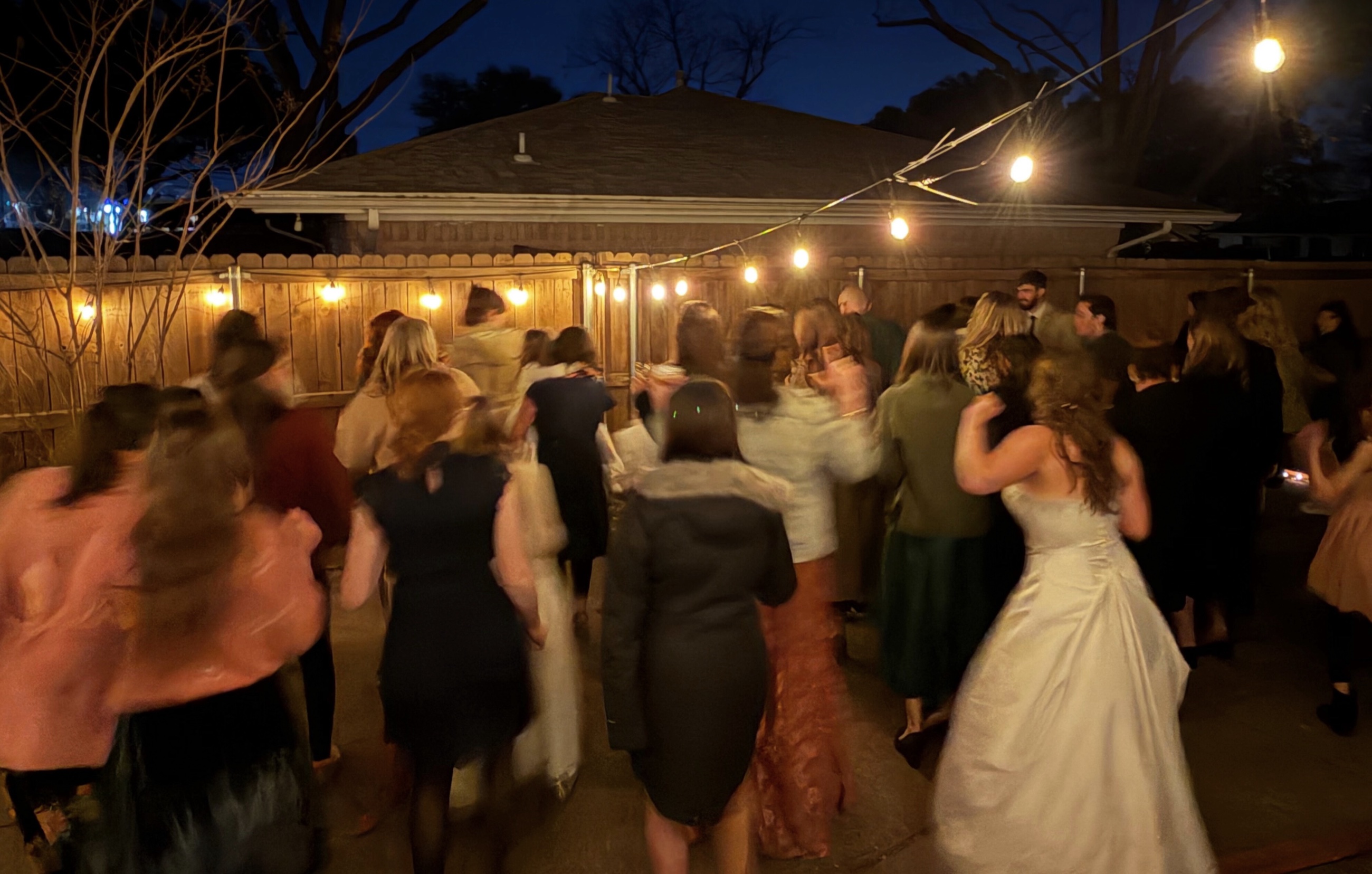 Wedding guests dancing outdoors under string lights at a backyard reception.