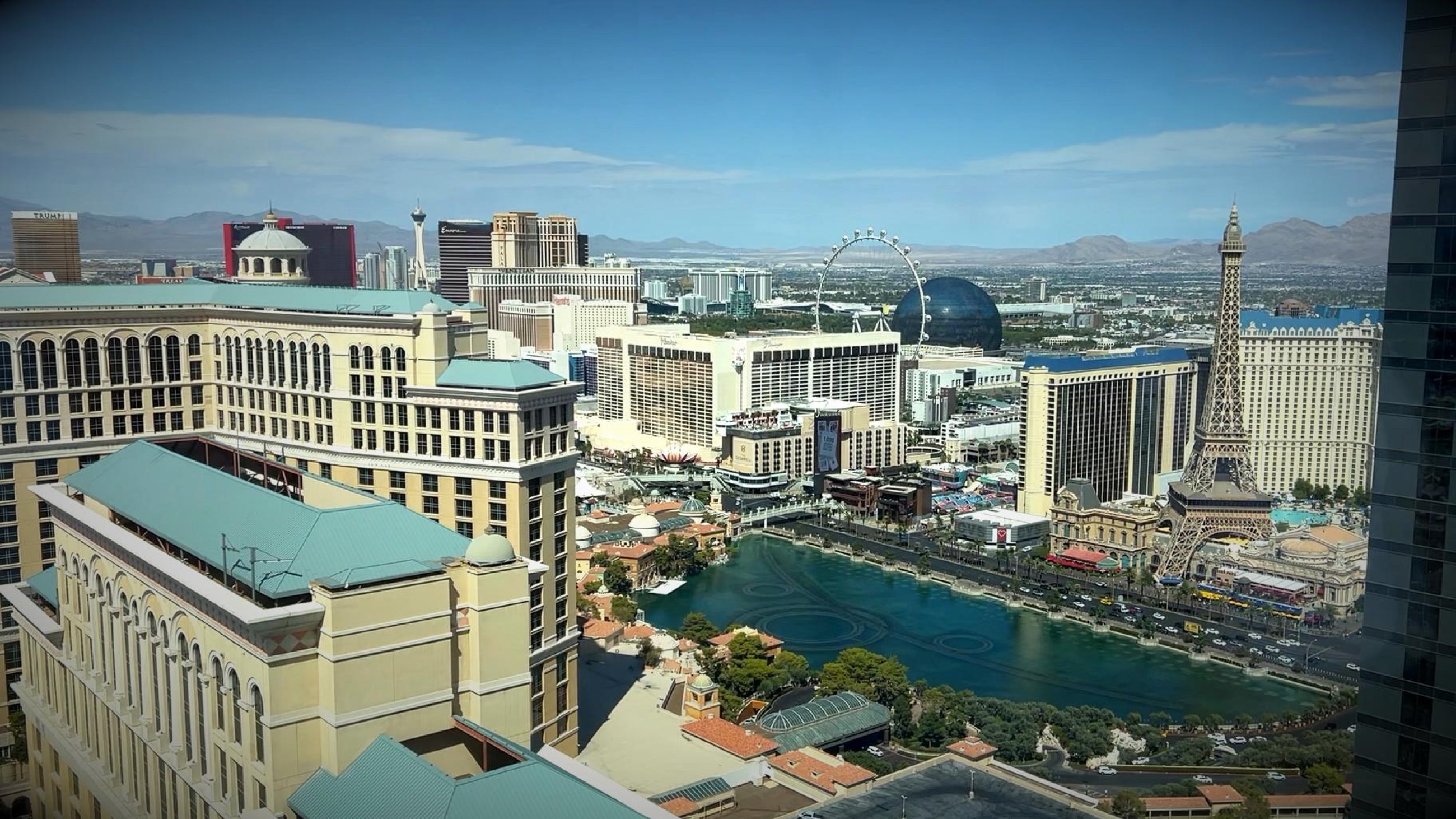 The Bellagio fountains, Paris Las Vegas, and desert mountains viewed from a high hotel room.