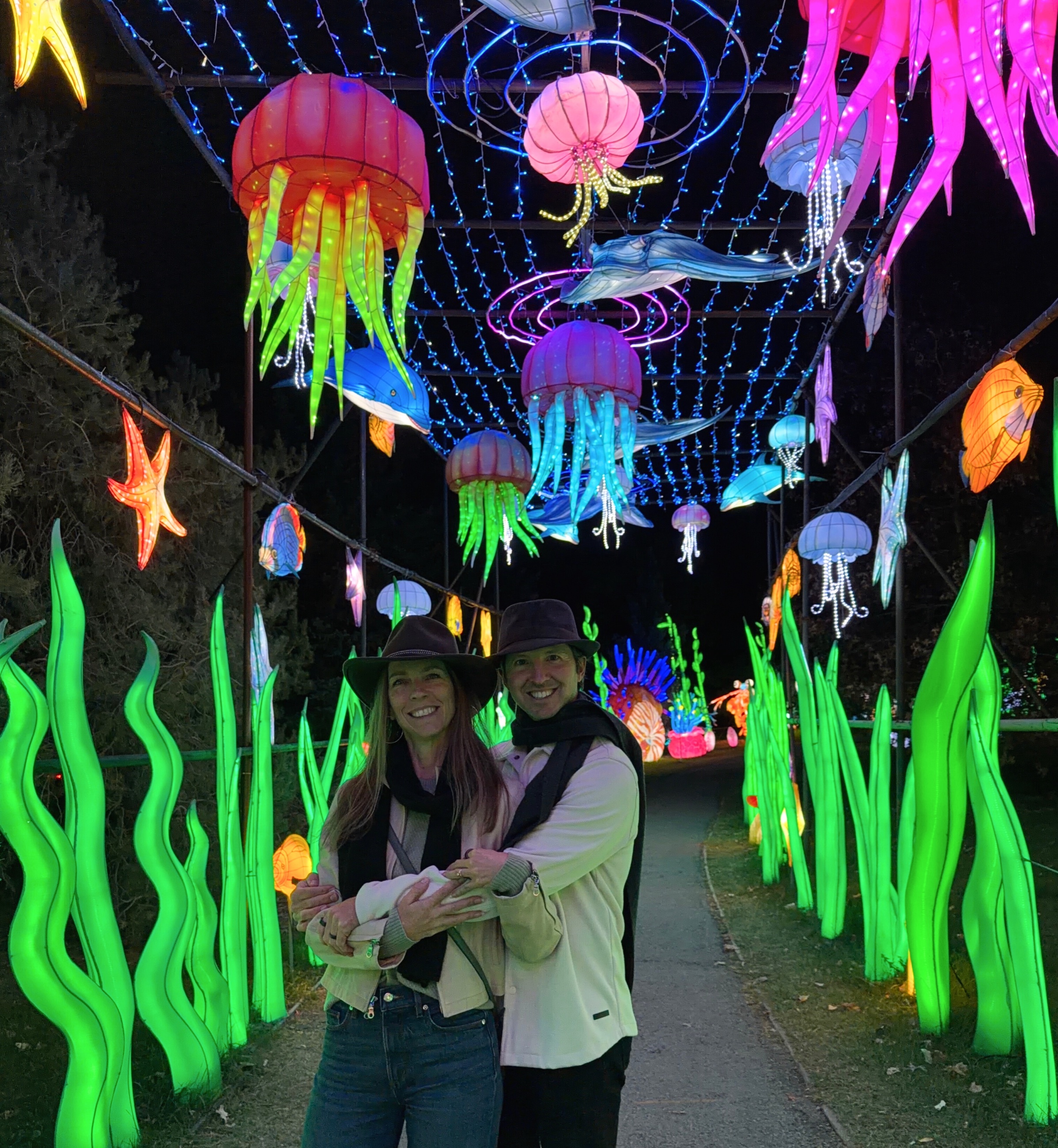 Sam and Stephanie standing beneath illuminated jellyfish along a lantern-lined path.