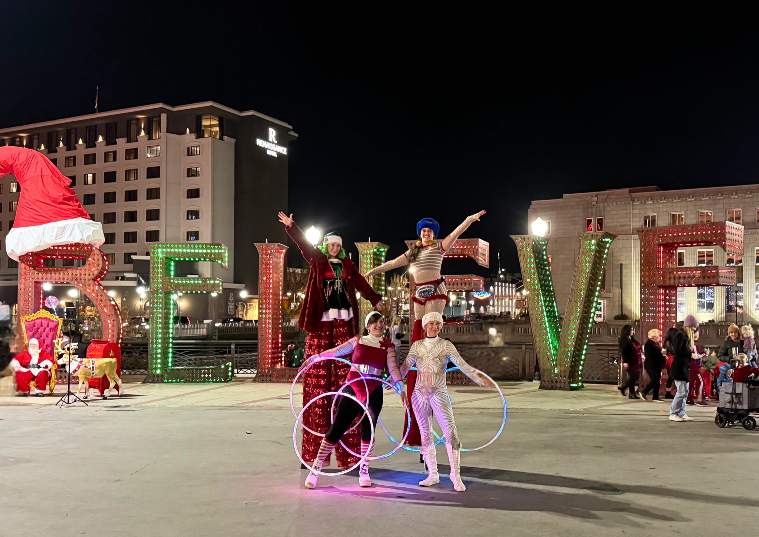 Holiday performers posing with illuminated BELIEVE letters at Reno City Plaza.
