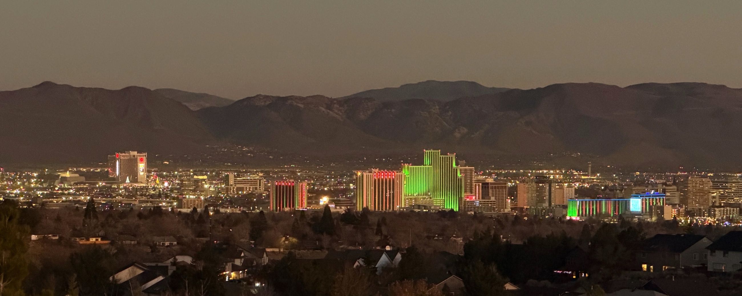 Downtown Reno illuminated at dusk beneath the dark outline of the surrounding mountains.