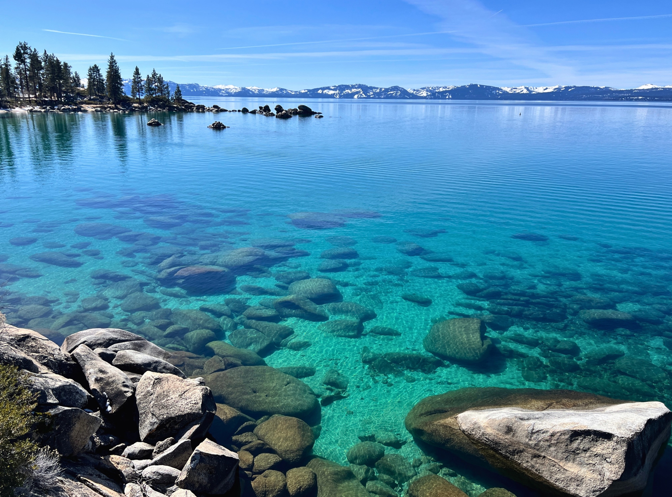 Clear Lake Tahoe water over granite with snow along the distant ridge