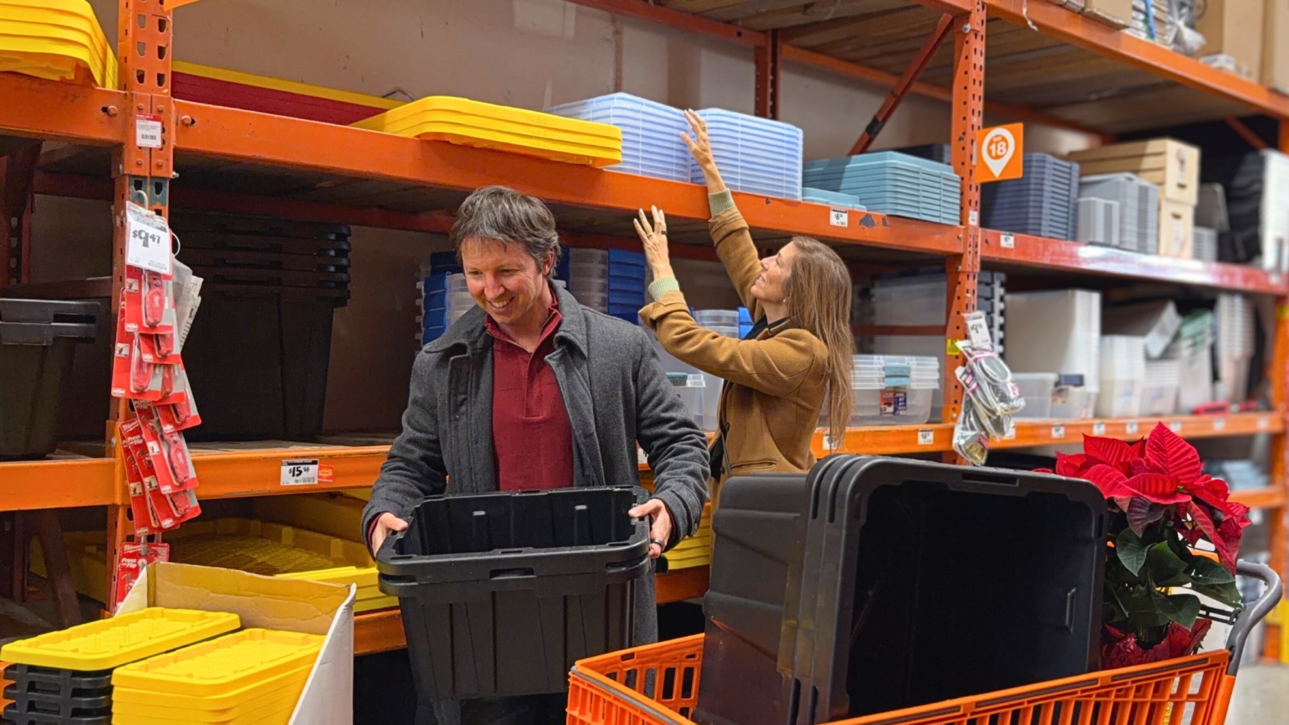Sam and Stephanie standing beside stacks of black-and-yellow storage bins inside Home Depot while preparing for their move.