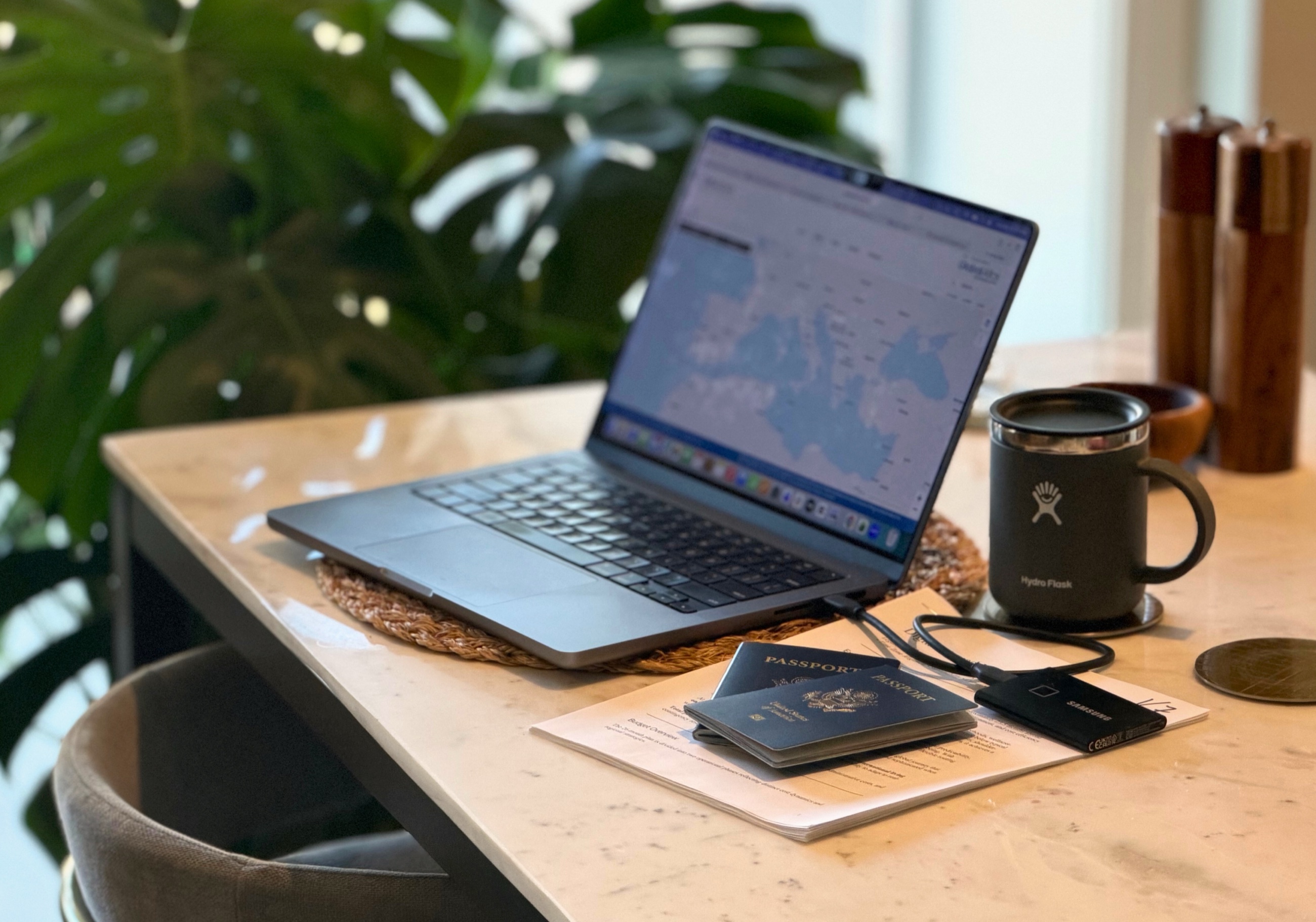 A laptop displaying route planning beside passports, a portable drive, notes, and coffee on a table.